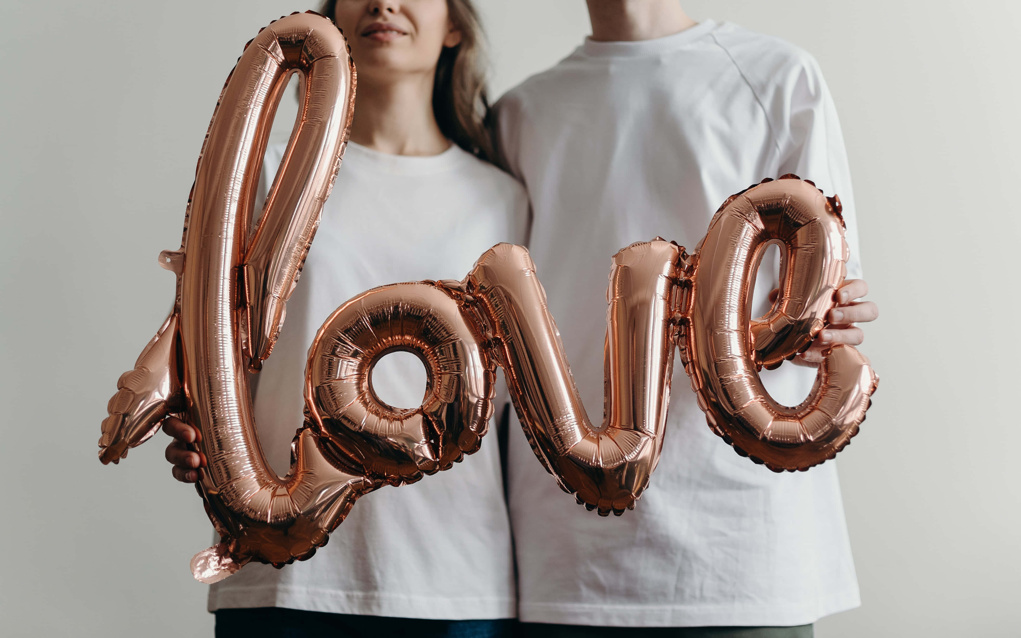 愛心 桌布 壁紙 — 一對情侶在純白色背景前手持拼出 'love' 的玫瑰金箔氣球。