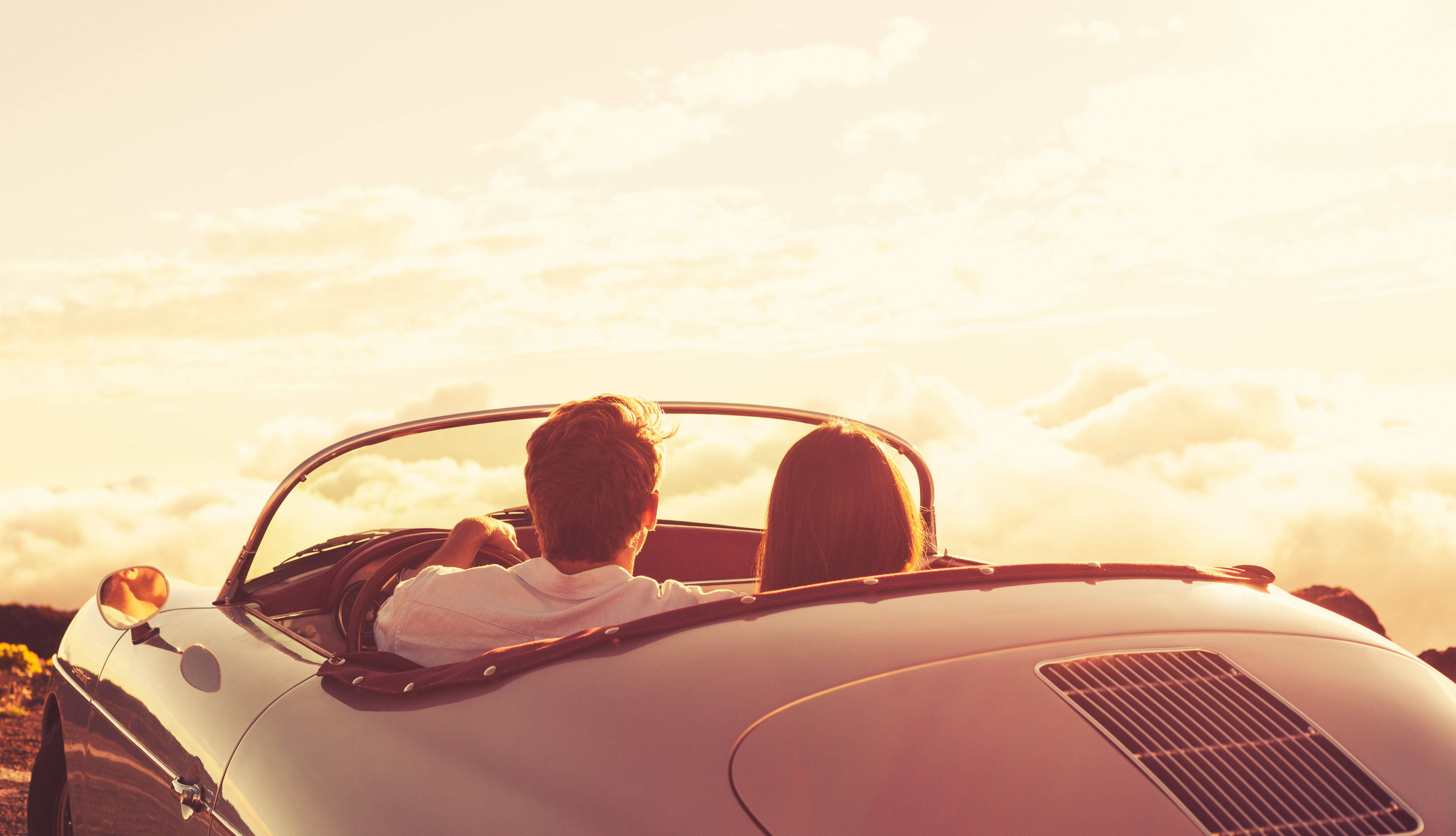 Love Story 桌布 壁紙 — 一對情侶在經典白色敞篷車上享受日落駕駛，位於山頂俯瞰蓬鬆的雲層。