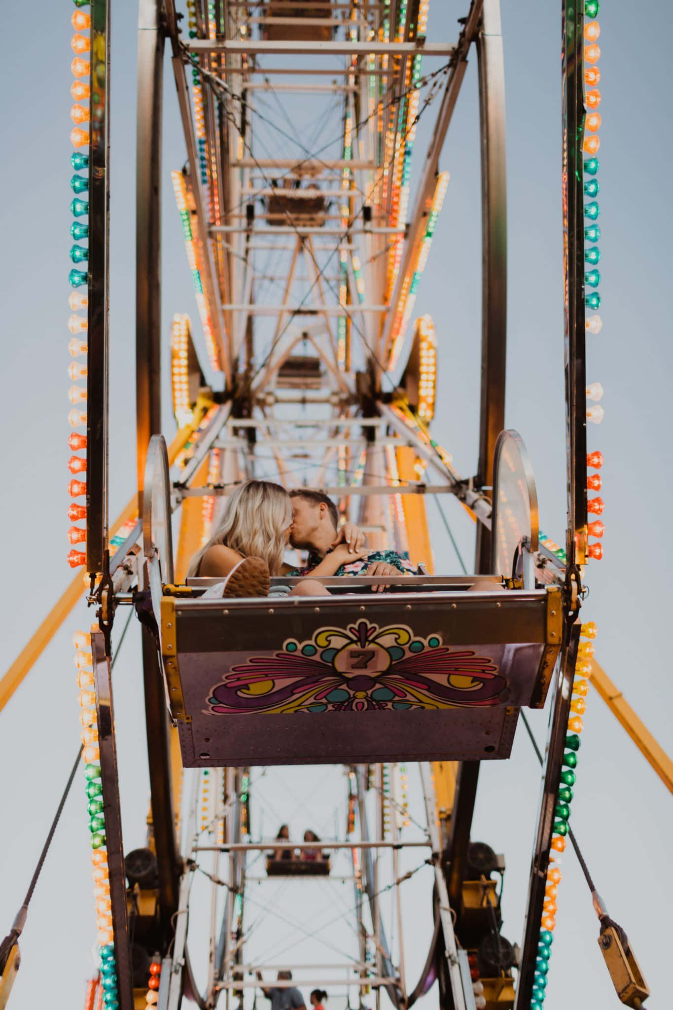 Carnival 桌布 壁紙 — 一對情侶在色彩繽紛的嘉年華摩天輪車廂內熱情接吻，背景是晴朗的天空。