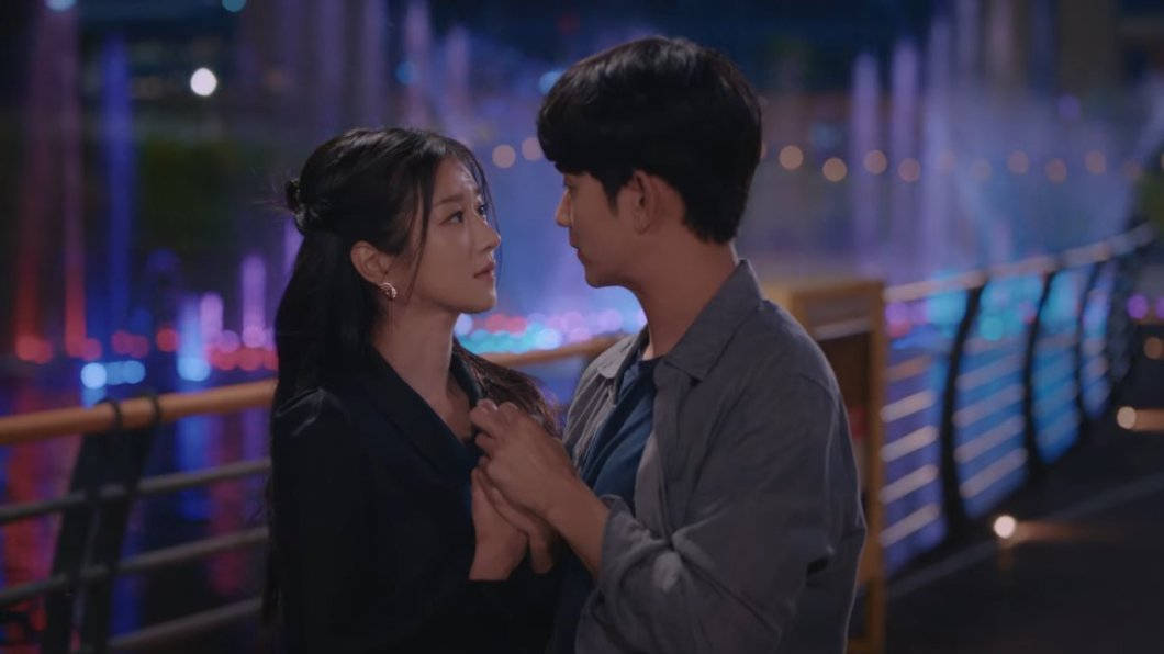 kdrama 桌布 壁紙 — 一對情侶在色彩繽紛的城市燈光下分享親密時刻，背景中的噴泉閃閃發光。