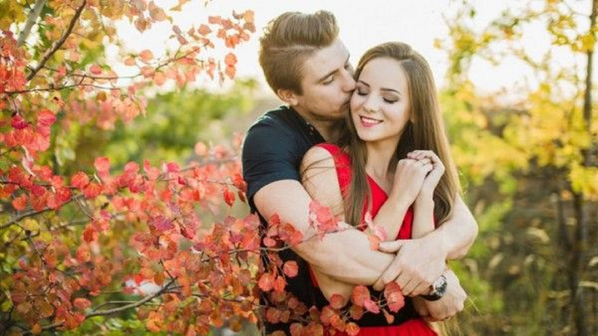 Romantic Love 桌布 壁紙 — 一對情侶在色彩繽紛的秋葉下溫暖擁抱，金色陽光穿過五彩斑斕的樹葉灑落。