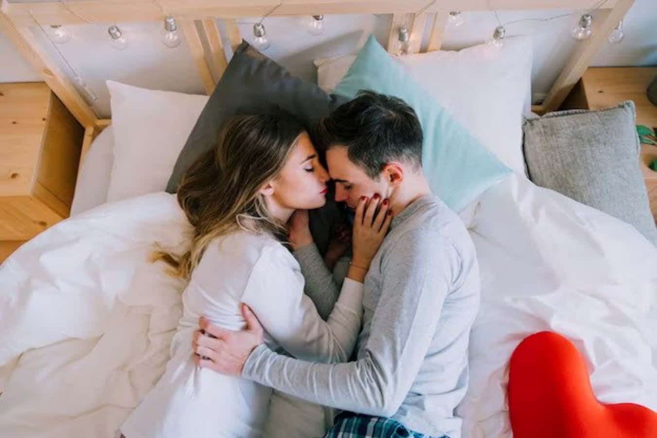 Kissing 桌布 壁紙 — 一對情侶在裝飾著燈串和柔軟枕頭的舒適床上分享親密時刻。