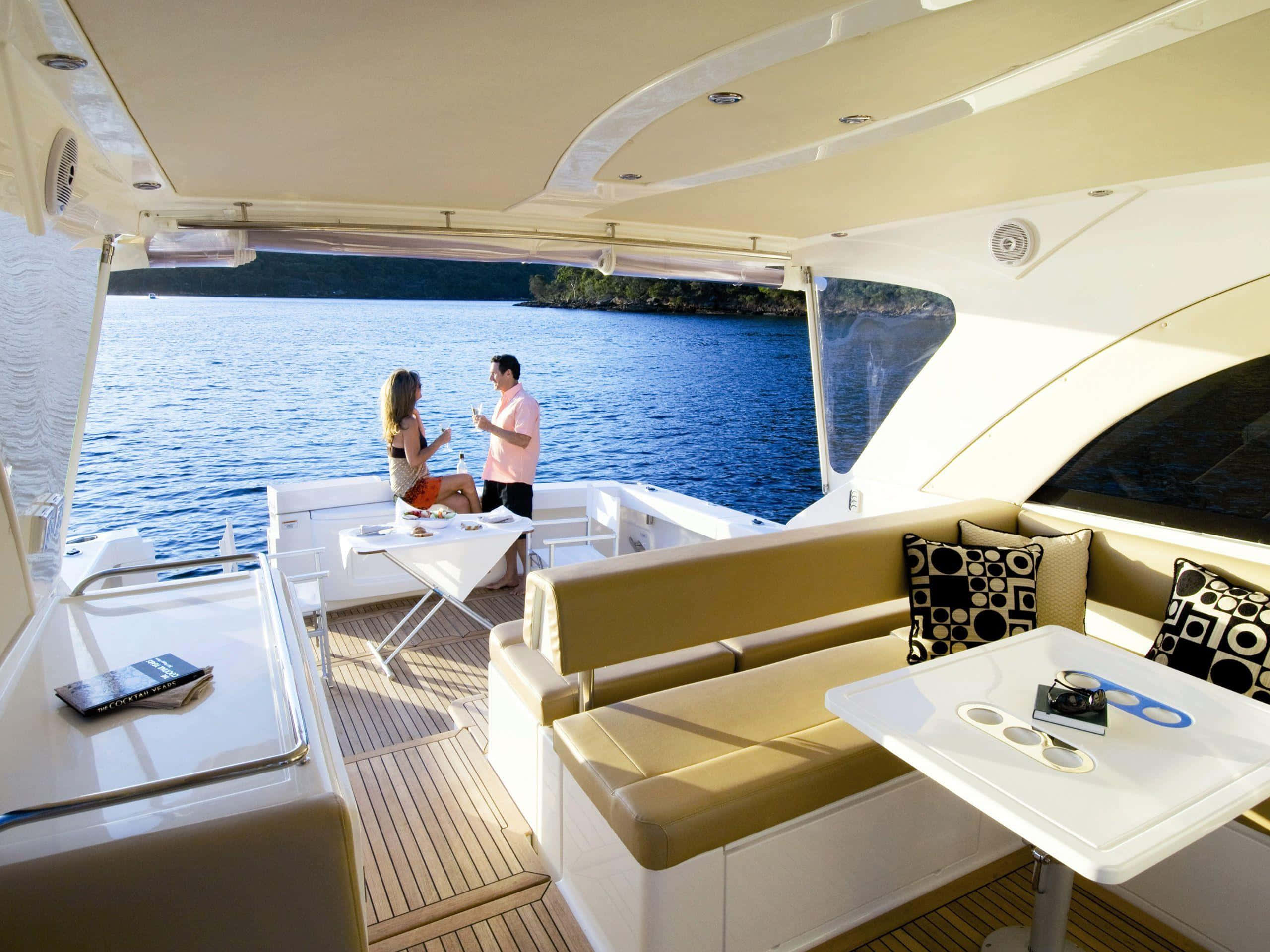 Yacht 桌布 壁紙 — 一對情侶在豪華遊艇甲板上享受飲品，俯瞰陽光下平靜的藍色海水。