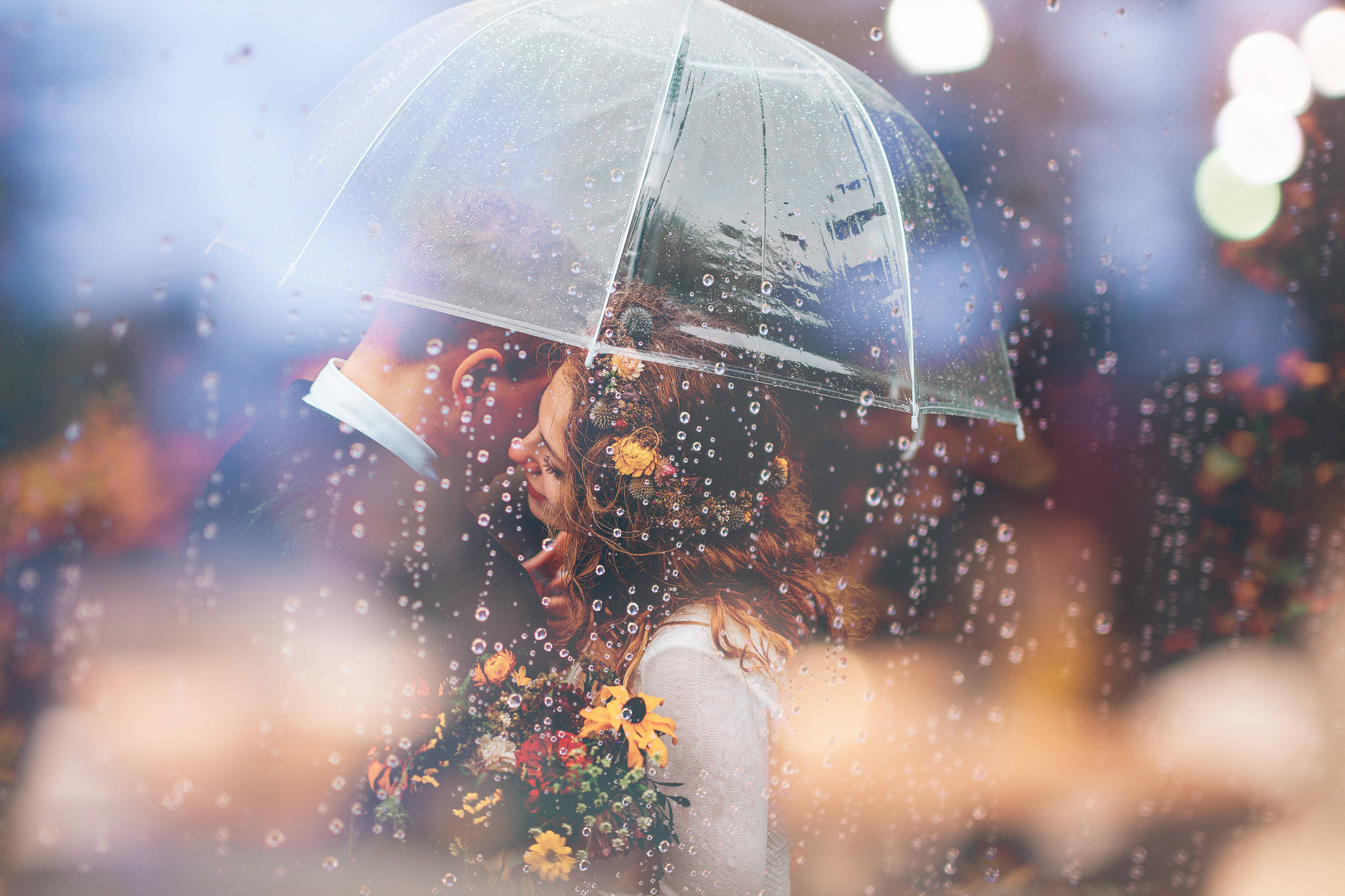 愛心 桌布 壁紙 — 一對情侶在透明雨傘下親吻，雨滴劃過玻璃，背景有溫暖的散景燈光閃爍。
