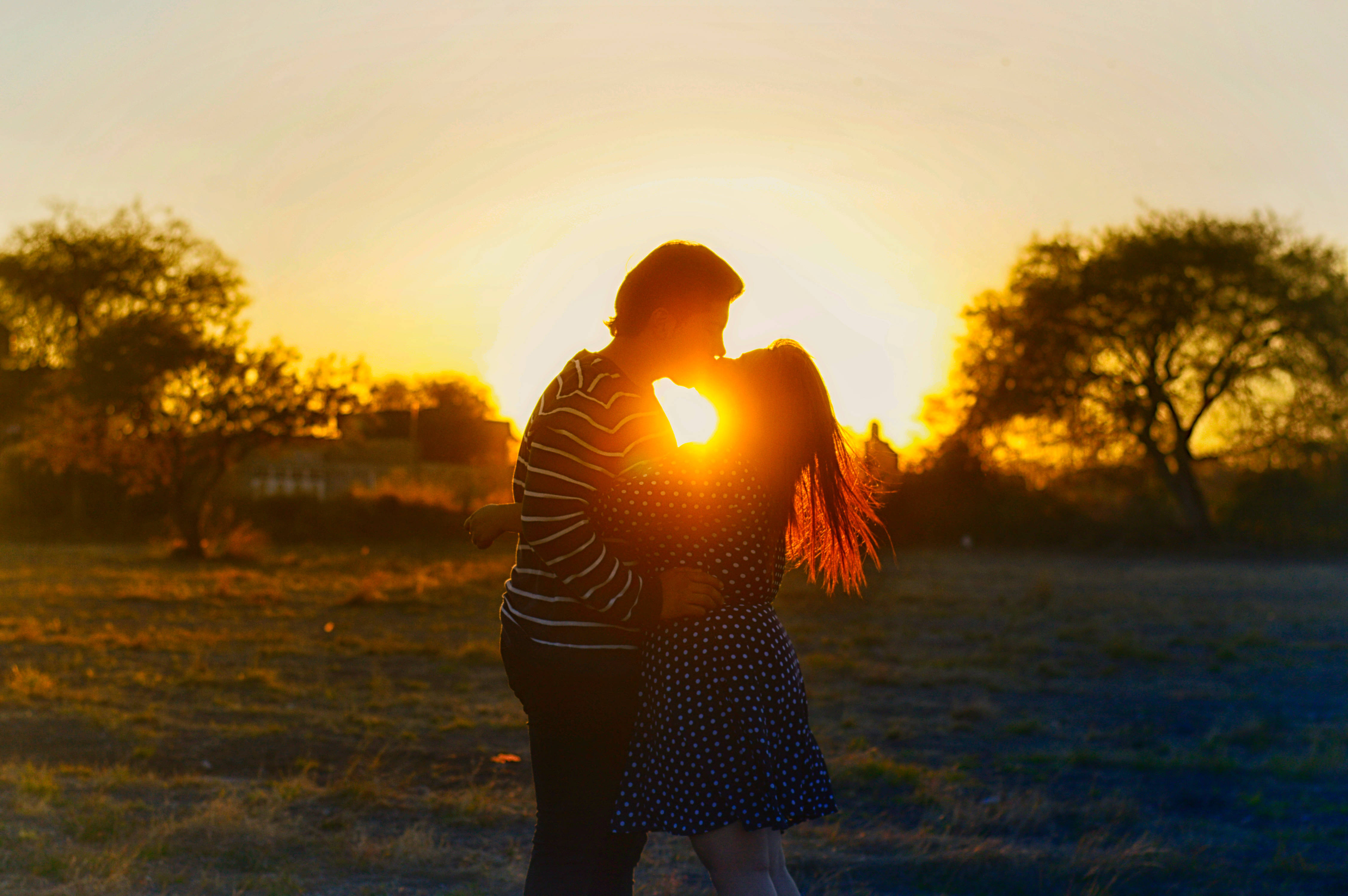 Love Cute Couple 桌布 壁紙 — 一對情侶在金色夕陽下擁抱，背景有樹木和草地，呈現剪影效果。