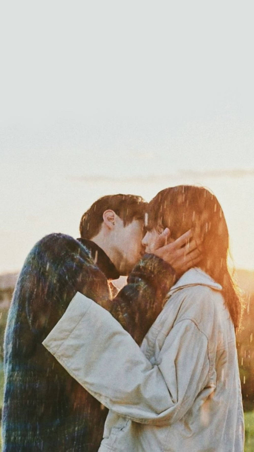 couple kiss 桌布 壁紙 — 一對情侶在金色日落時分，於雨中親吻，伴隨著柔和溫暖的光線。