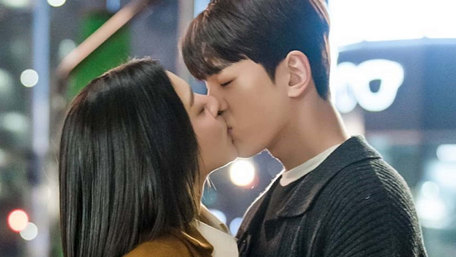 Kissing 桌布 壁紙 — 一對情侶在閃爍的城市燈光下親吻，背景是模糊的霓虹燈牌。