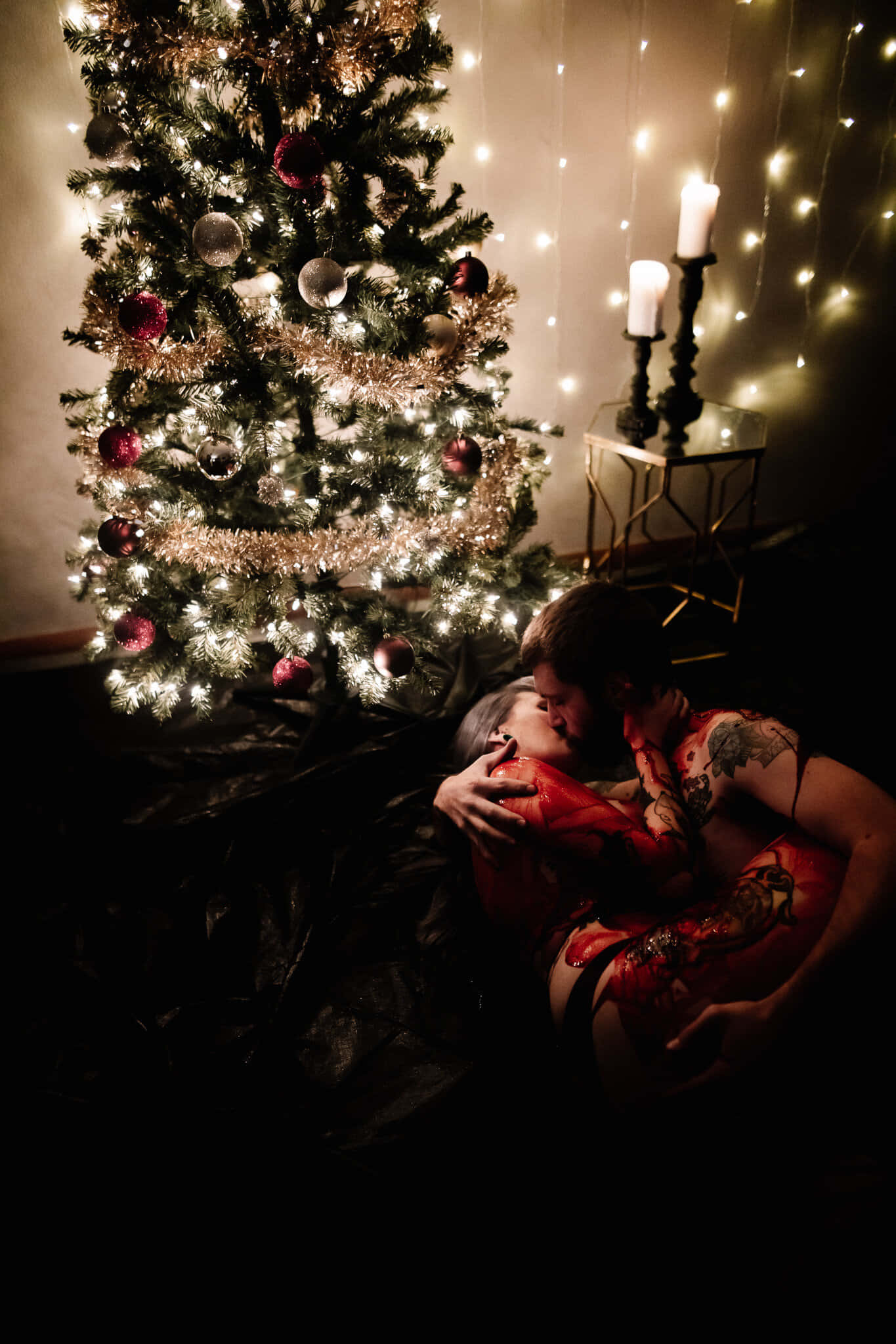 Couples Christmas 桌布 壁紙 — 一對情侶在閃爍的聖誕樹下溫柔擁抱，樹上裝飾著紅色飾物和閃爍的燈光。