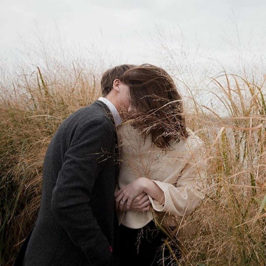 Aesthetic Couple 桌布 壁紙 — 一對情侶在陰天下的高聳金色草叢中溫柔擁抱。