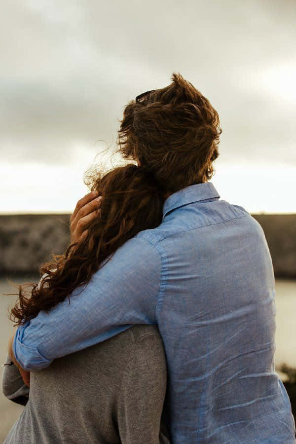 Hugging 桌布 壁紙 — 一對情侶在陰天從後擁抱，俯瞰水面，柔和自然光。