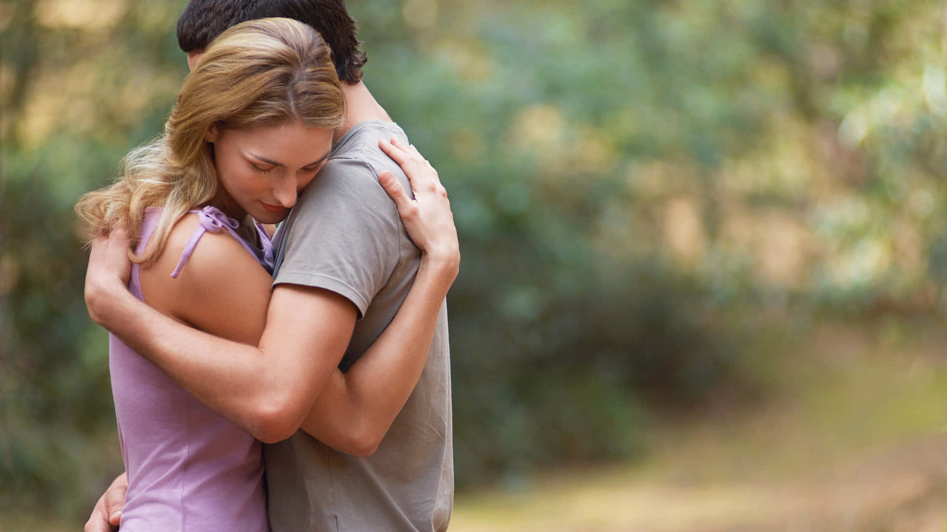 Hug 桌布 壁紙 — 一對情侶在陽光明媚的森林中溫柔擁抱，背景是柔和模糊的綠色植物。