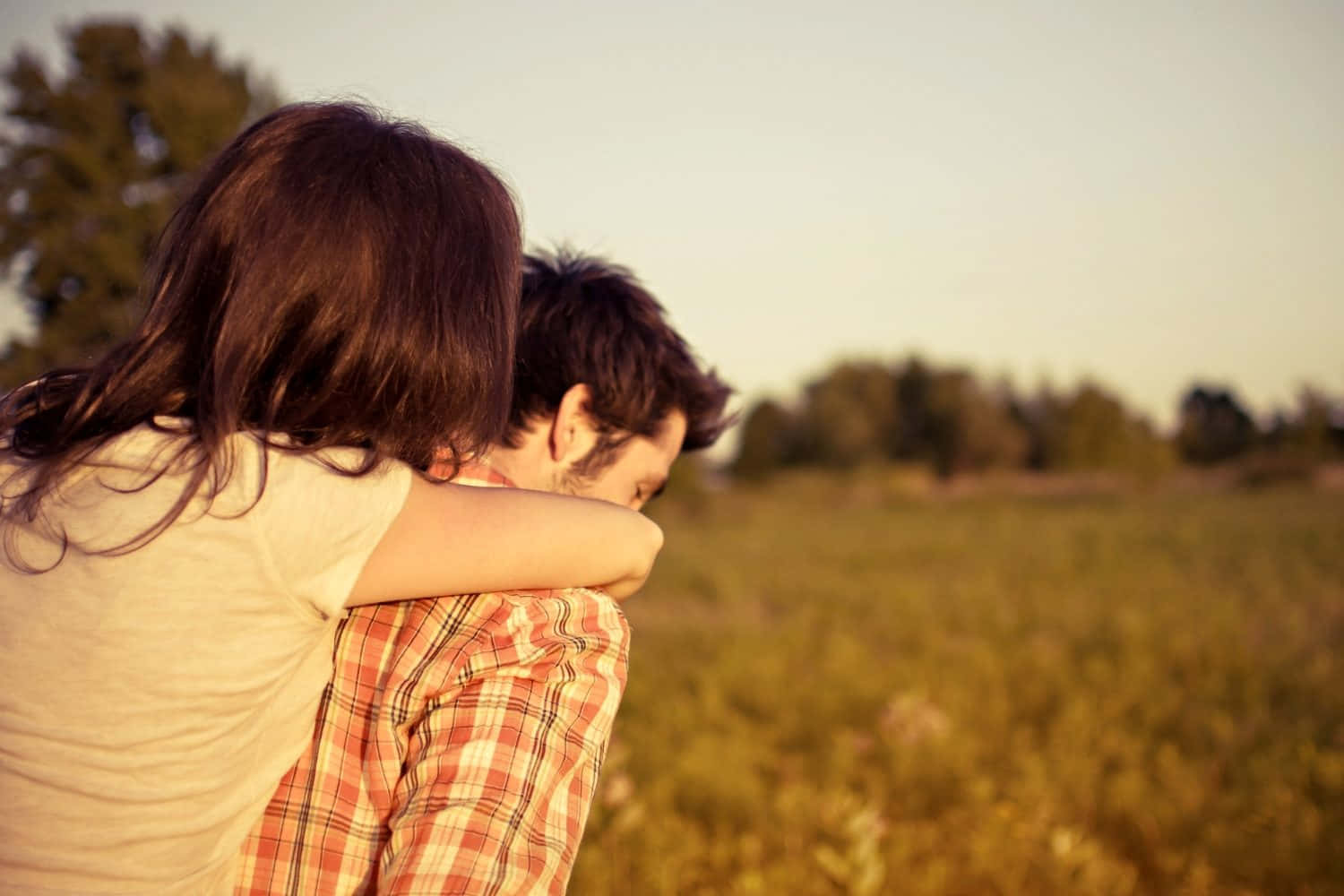 Relationship Cute Couple 桌布 壁紙 — 一對情侶在陽光明媚的田野中於黃金時刻溫暖擁抱，背景是柔和模糊的樹木。