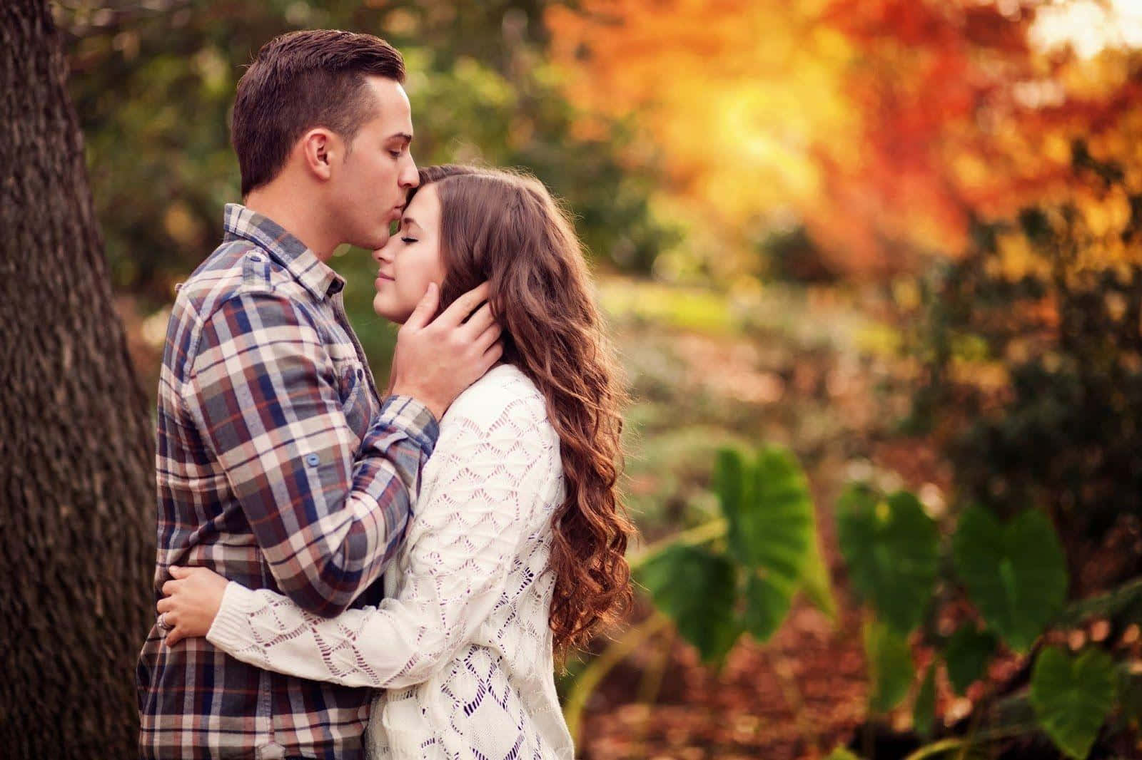 Romantic Love 桌布 壁紙 — 一對情侶在陽光明媚的秋日森林中親吻，周圍是鮮豔的橙色樹葉。