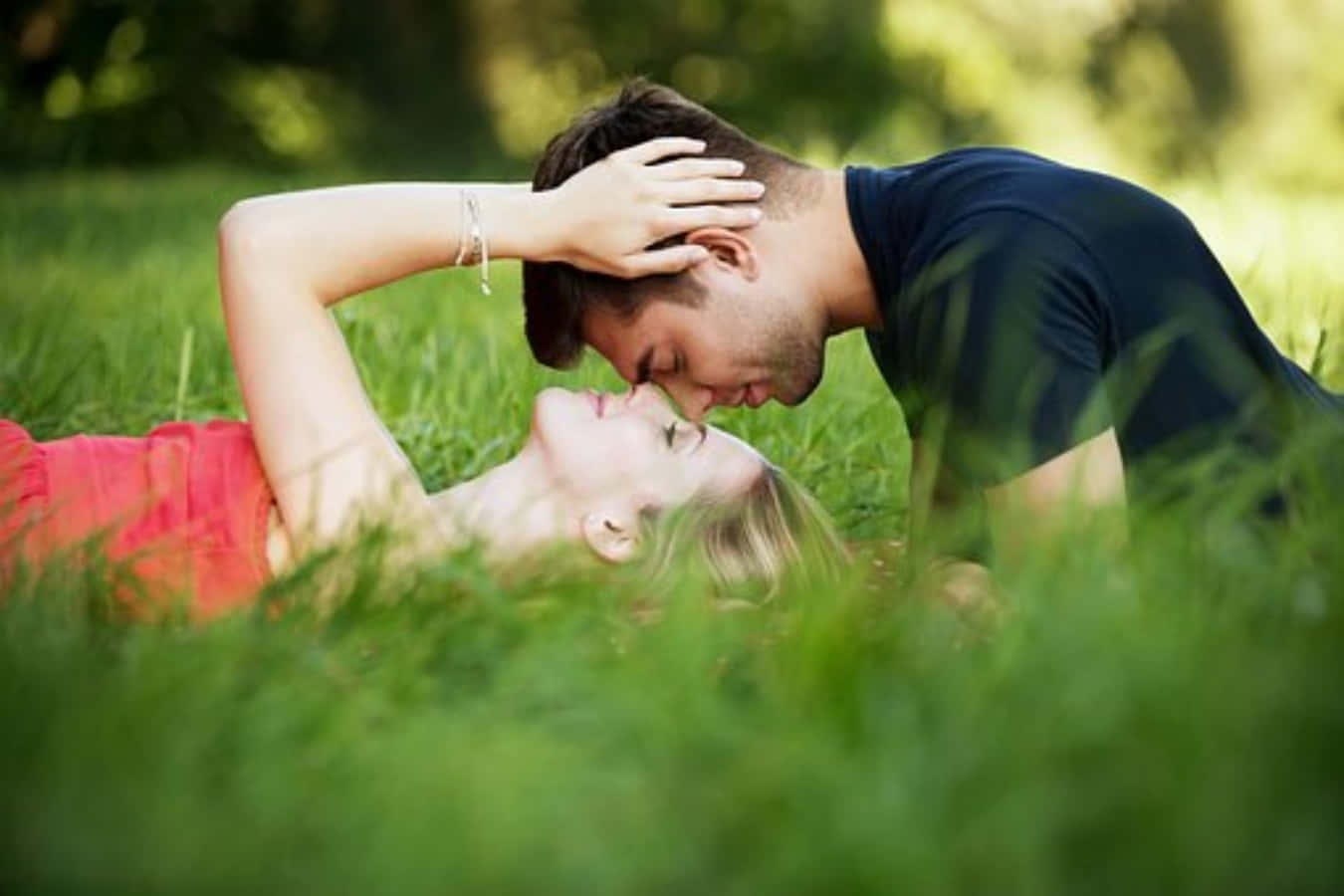 lover 桌布 壁紙 — 一對情侶在陽光明媚的草地上親密地躺在一起，身後是模糊的綠色樹葉。