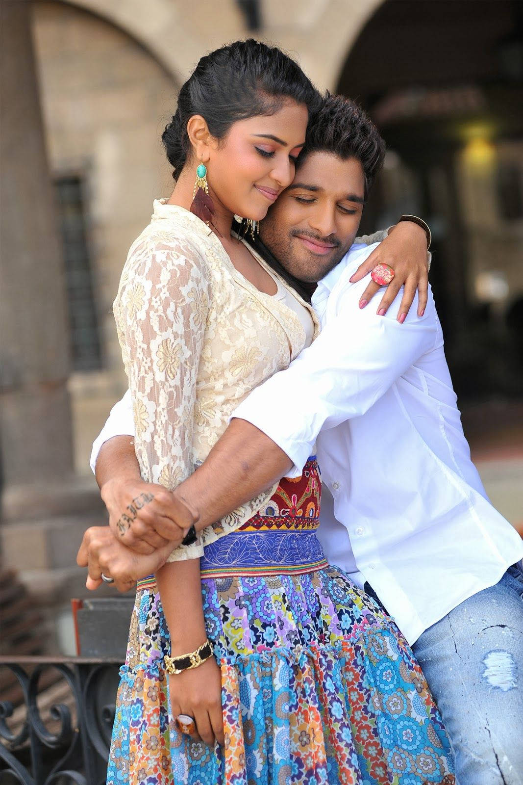 Allu Arjun 桌布 壁紙 — 一對情侶在陽光普照的城市庭院中溫柔擁抱，身後有石拱門和華麗的欄杆。