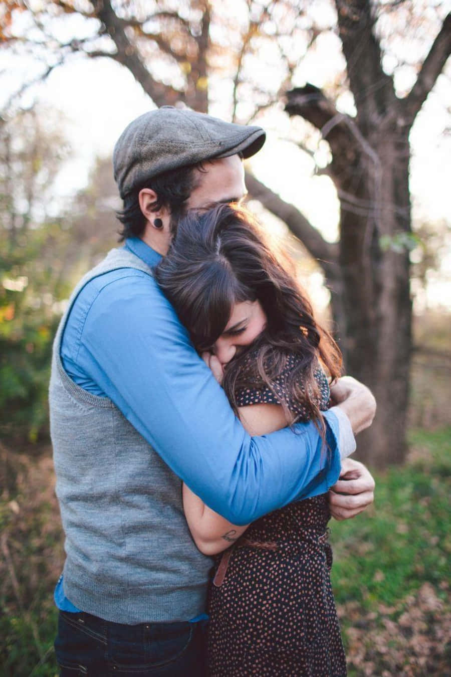 Hug 桌布 壁紙 — 一對情侶在陽光普照的森林中溫柔擁抱，樹木光禿，金色光線穿過樹枝。