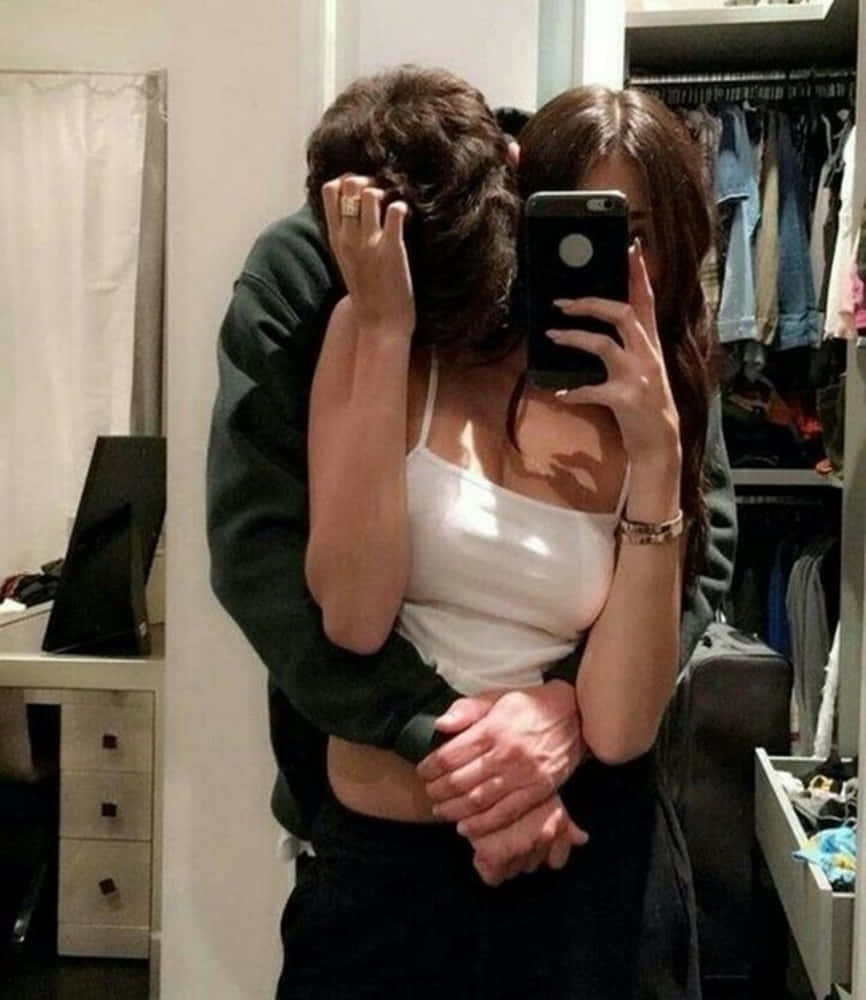 Girlfriend And Boyfriend 桌布 壁紙 — 一對情侶在雜亂的臥室中，衣架和傢俱可見，對著鏡子自拍擁抱。