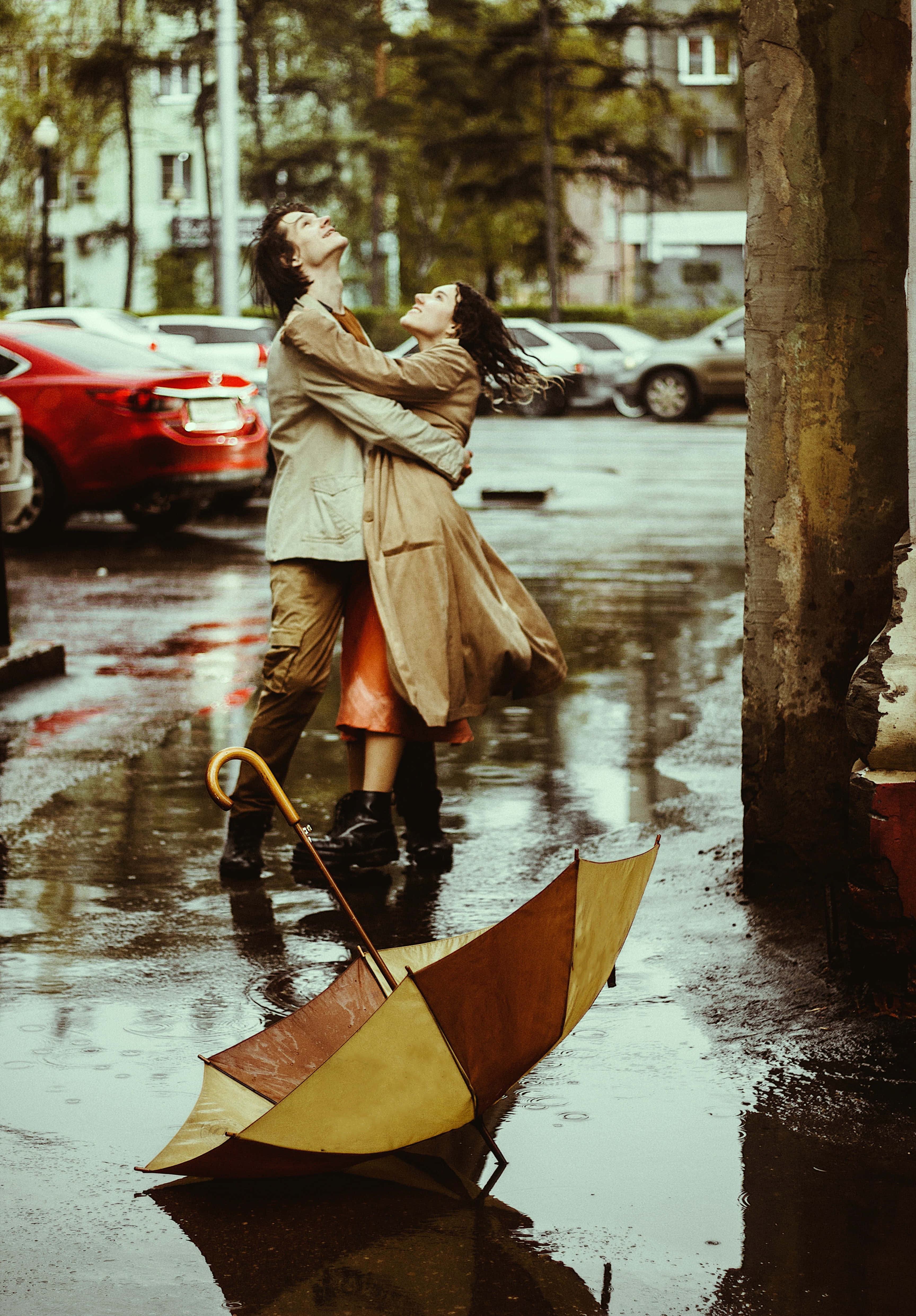Umbrella 桌布 壁紙 — 一對情侶在雨中快樂地擁抱，一把色彩繽紛的雨傘被遺棄在濕漉漉的人行道上。