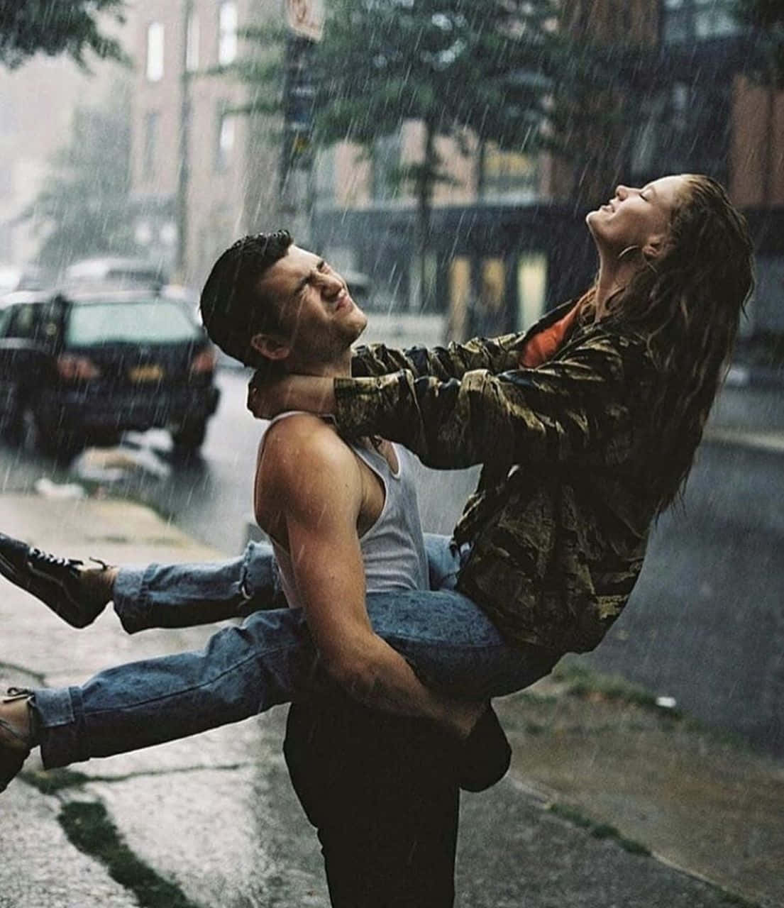 Couple In Rain 桌布 壁紙 — 一對情侶在雨中快樂地擁抱，背景是濕漉漉的街道和模糊的汽車。
