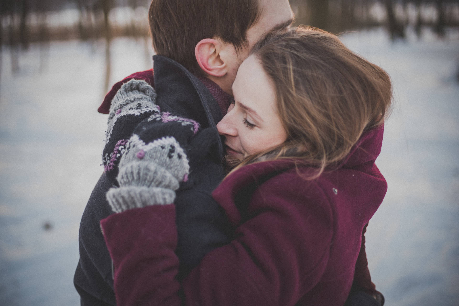 壁紙 — 一對情侶在雪地中溫暖擁抱，柔和冬日光線和低調色調。
