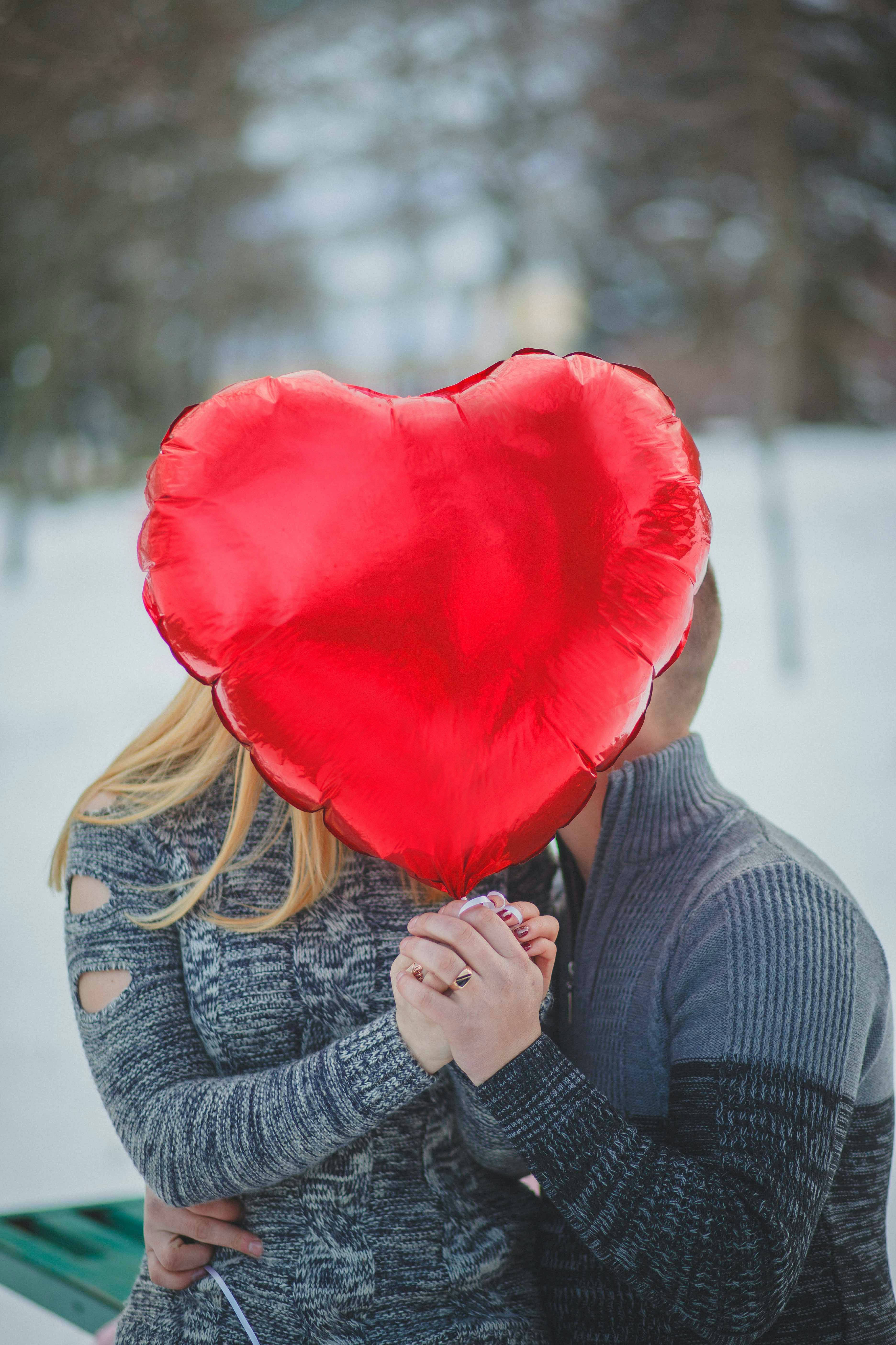 Love Heart 桌布 壁紙 — 一對情侶在雪地公園擁抱，一個大紅色心形氣球遮蓋了他們的臉。