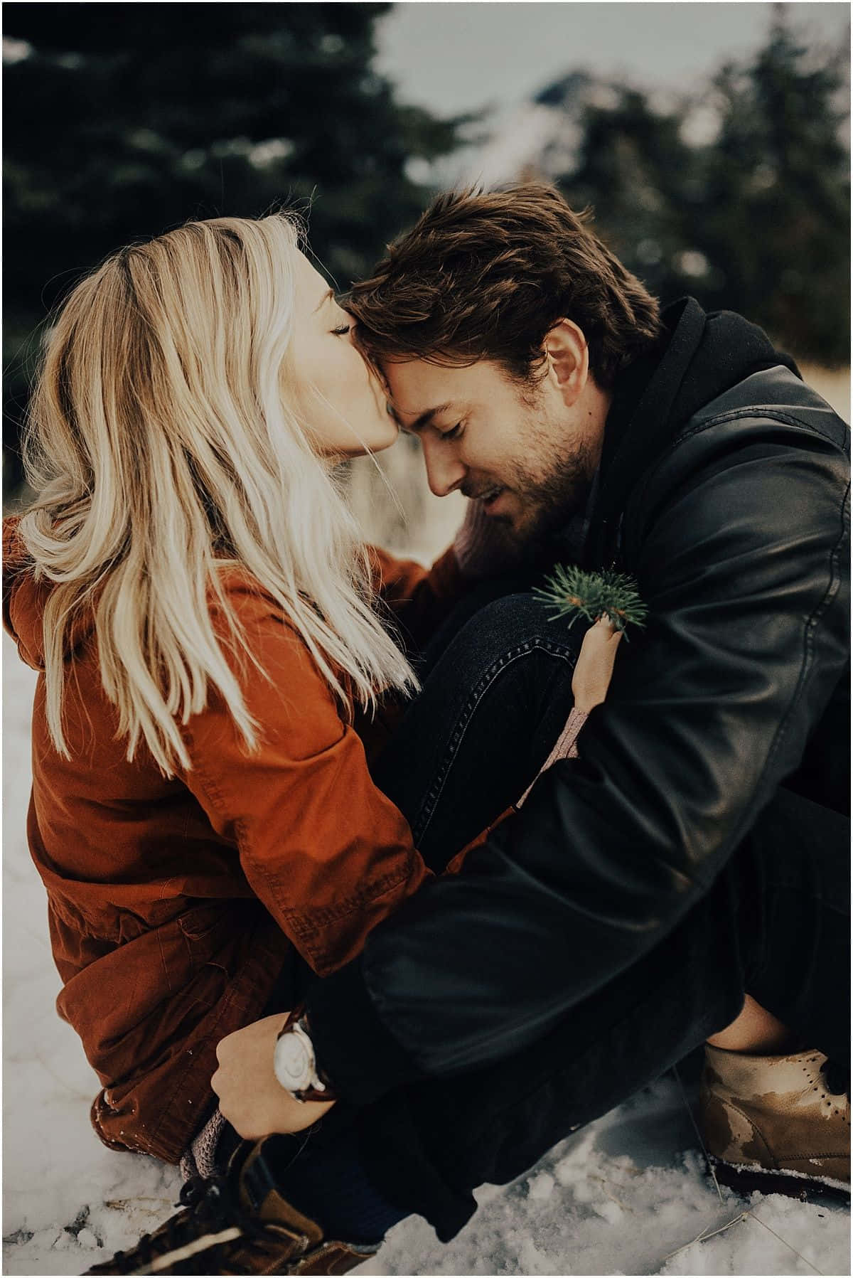 Forehead Kiss 桌布 壁紙 — 一對情侶在雪地森林中，松樹和柔和冬日陽光下，分享一個溫柔的親吻。