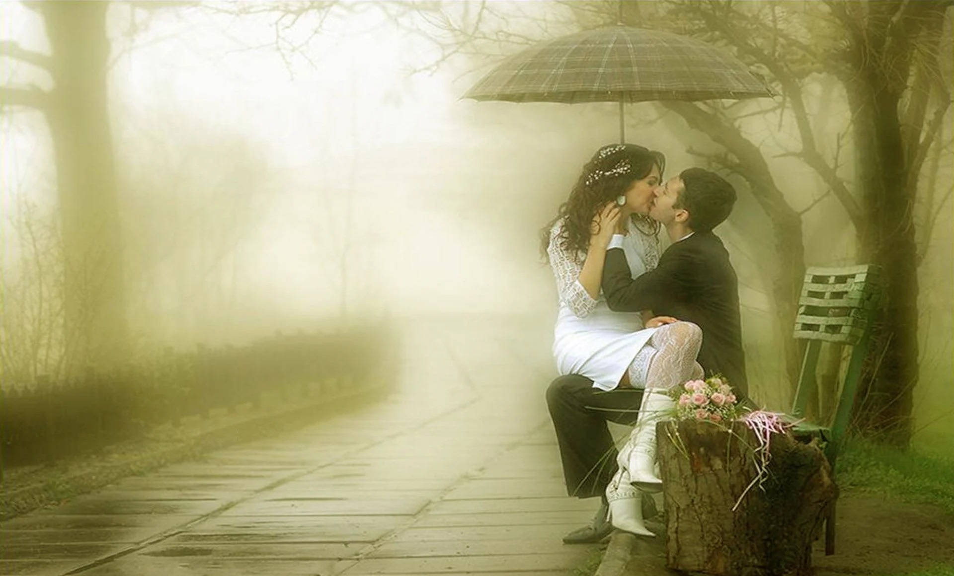 Romantic Love 桌布 壁紙 — 一對情侶在霧氣瀰漫的公園長椅上，於黑色雨傘下親吻，柔和的金色光線穿過光禿的樹木。