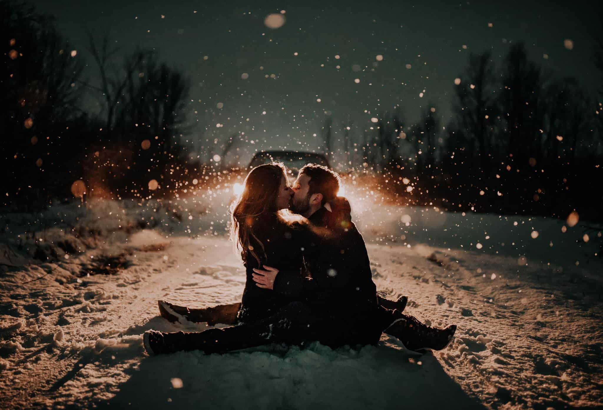 Beautiful Couple 桌布 壁紙 — 一對情侶在飄雪中親吻，溫暖的背光映襯著黑暗的冬日景色。