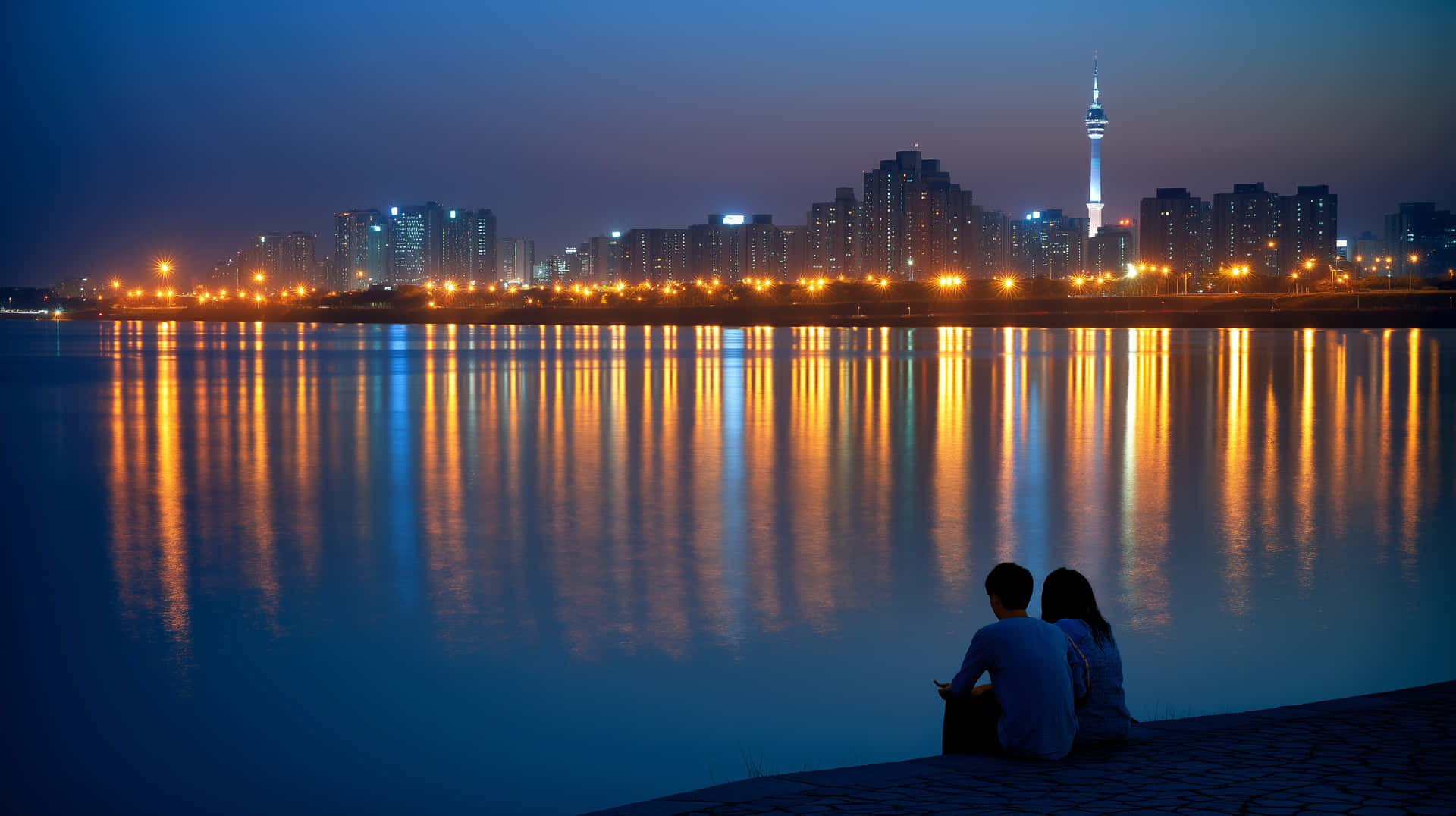City Lights on Water: Couple's Quiet Evening by River 壁紙 — 一對情侶在黃昏時分以剪影形式坐在河邊，觀看城市燈光倒映在平靜的水面上，遠處有一座高塔在發光。