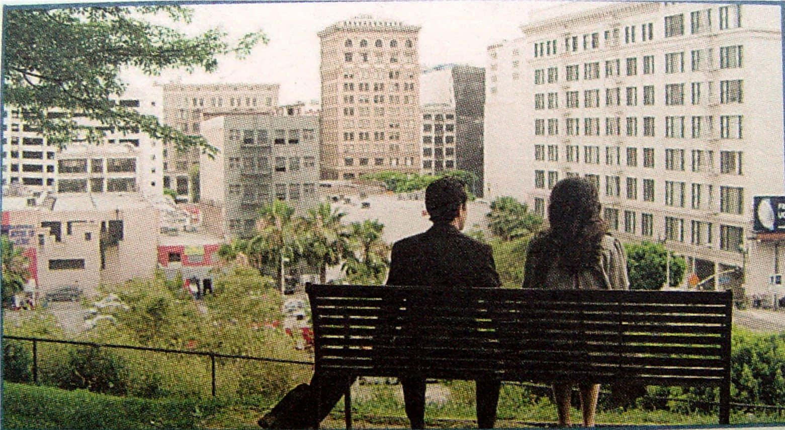 500 Days Of Summer 桌布 壁紙 — 一對情侶坐在長椅上，俯瞰著明亮的天空下高樓大廈和棕櫚樹的城市景觀。