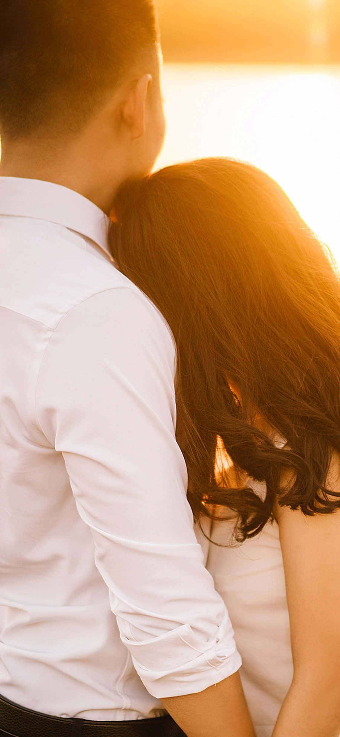 Relationship 桌布 壁紙 — 一對情侶從後溫暖地擁抱，金色夕陽灑滿他們的頭髮和白色襯衫。