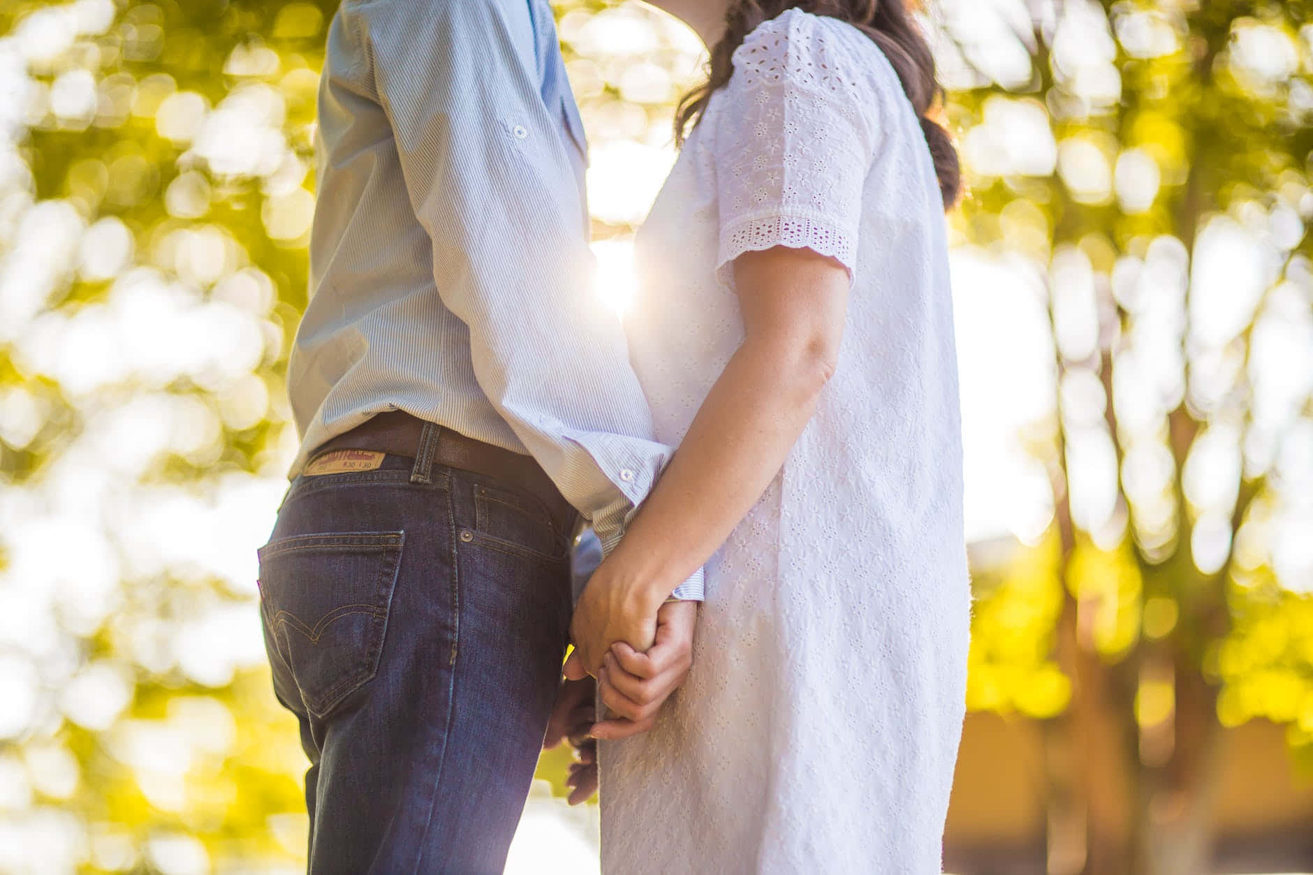 couple love 桌布 壁紙 — 一對情侶從背後牽手，金色陽光穿過樹木，溫暖地擁抱著。