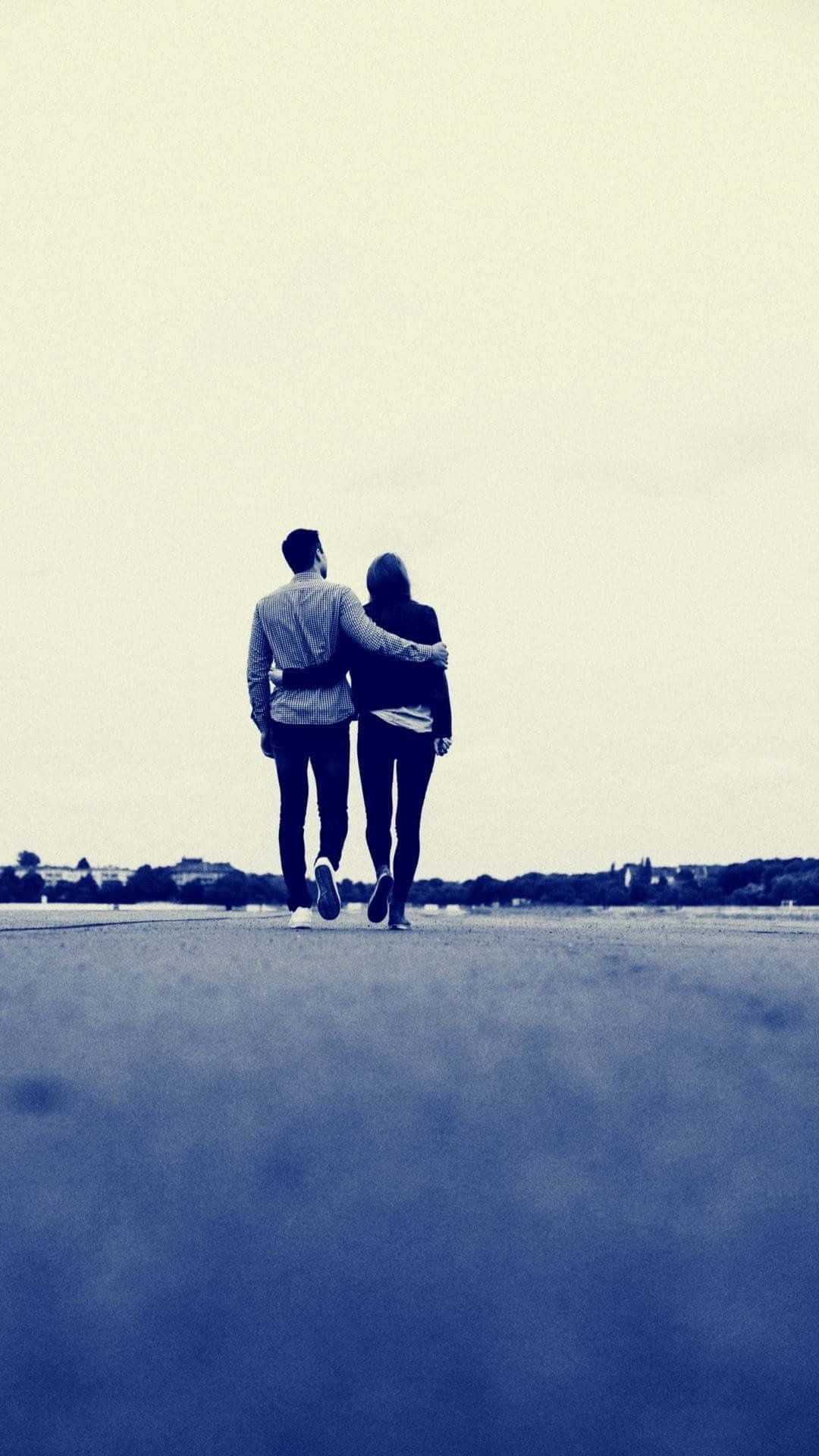 Relationship Cute Couple 桌布 壁紙 — 一對情侶手挽手沿著一條寬闊的道路行走，天空蒼白，遠處有樹木和建築物。