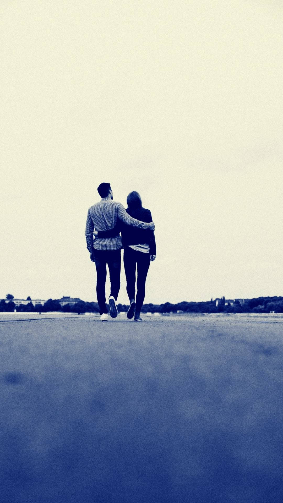 Love Story 桌布 壁紙 — 一對情侶手挽手走在一條寬闊開闊的道路上，天空蒼白，地平線上有遠處的樹木。