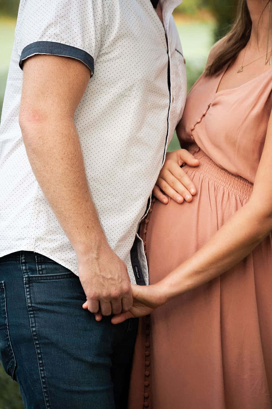 Pregnant 桌布 壁紙 — 一對情侶手牽手，男人的手臂環繞著孕婦的腰，在戶外溫馨的時刻。