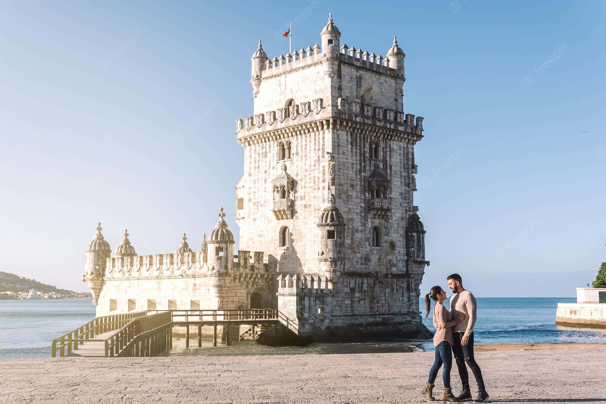 Portugal 桌布 壁紙 — 一對情侶手牽手在歷史悠久的貝倫塔旁的石碼頭上散步，天空晴朗蔚藍。