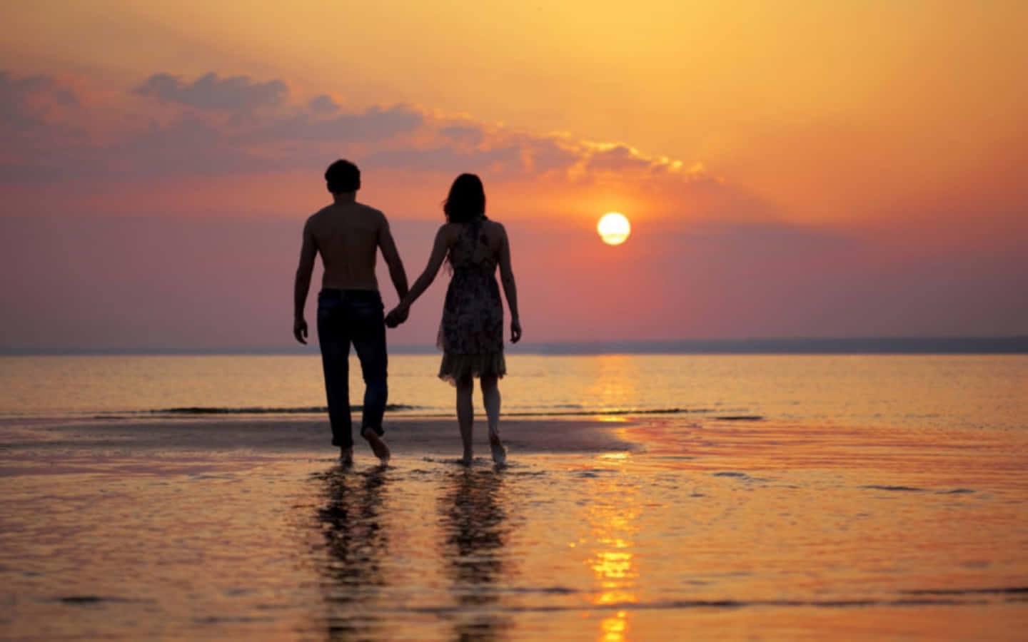 Romantic Love 桌布 壁紙 — 一對情侶手牽手沿著濕漉漉的海灘漫步，夕陽以火熱的橙色和粉紅色調落下。