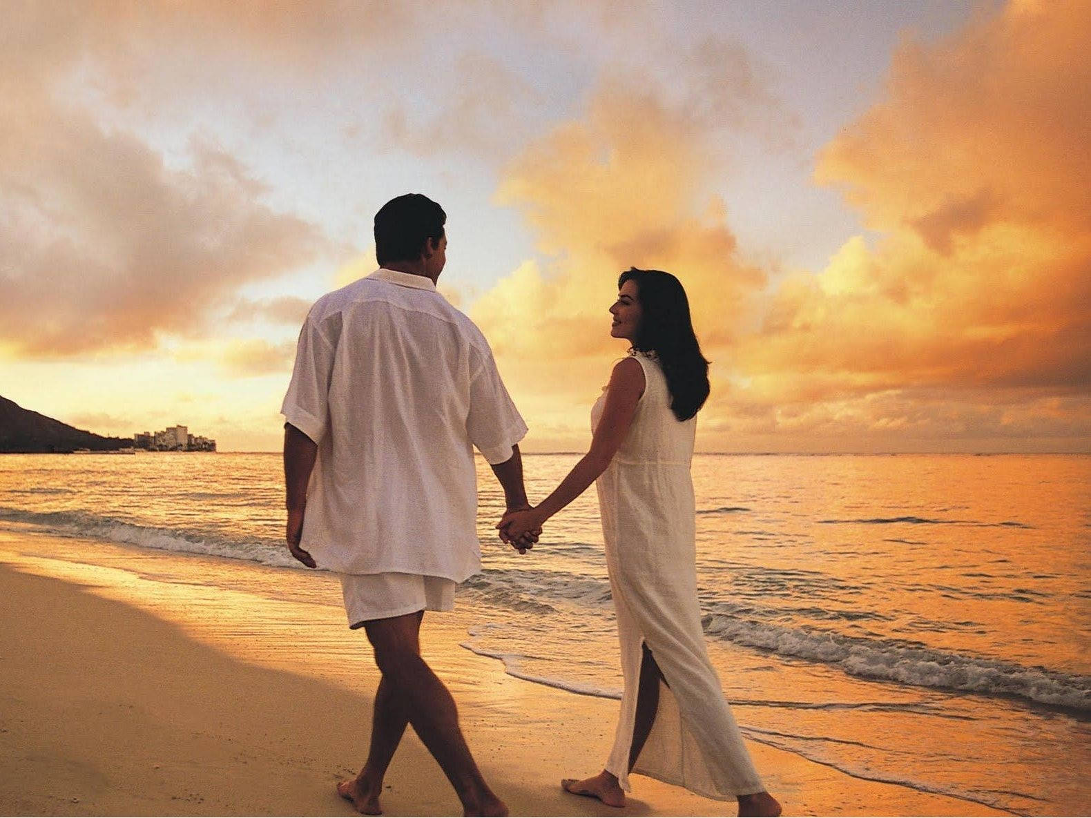Couples 桌布 壁紙 — 一對情侶手牽手沿著金色沙灘漫步，夕陽西下，溫暖的橙色雲彩在上方。