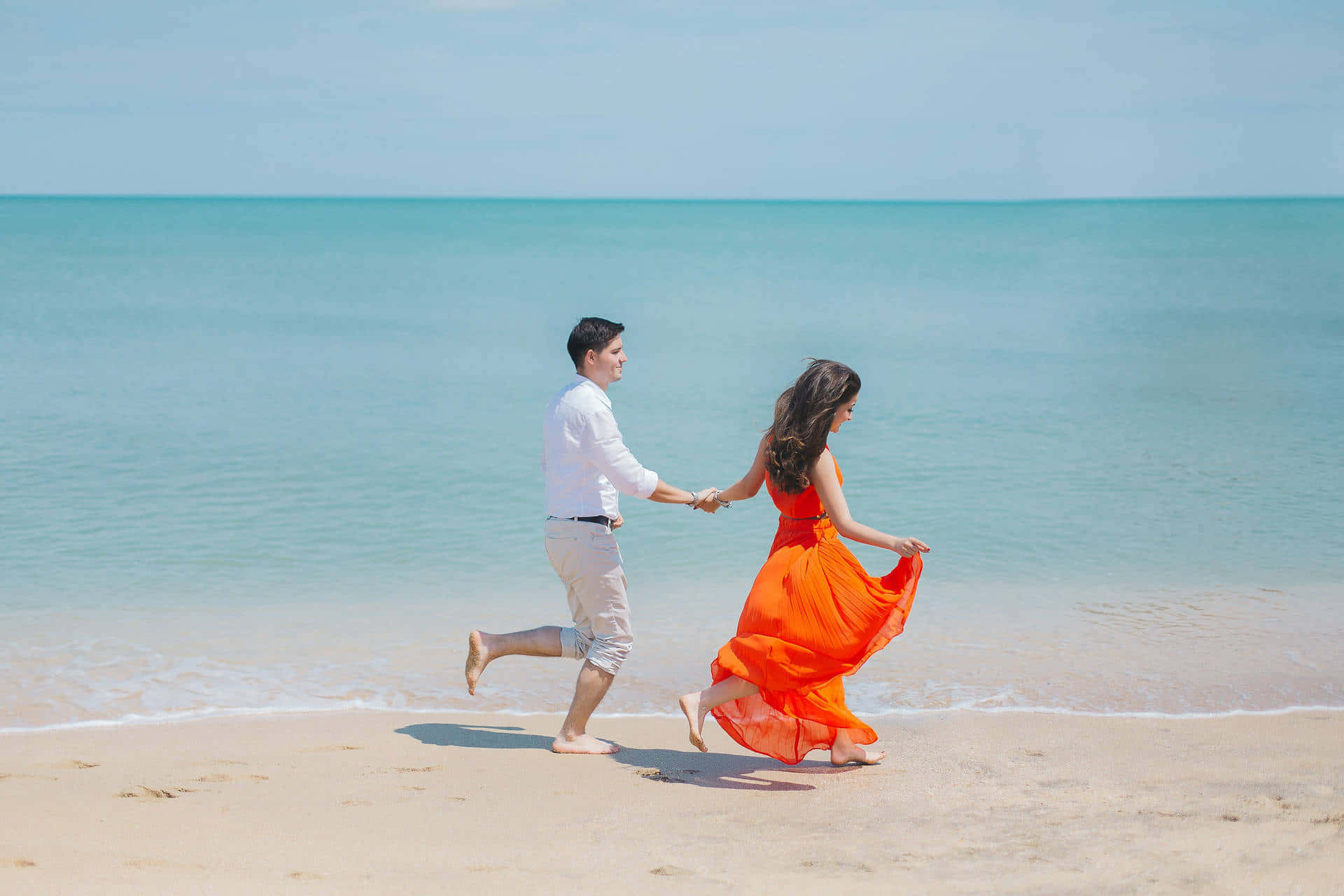 Romantic Love 桌布 壁紙 — 一對情侶手牽手沿著陽光明媚的海灘奔跑，碧綠的海浪輕輕拍打著金色的沙灘。