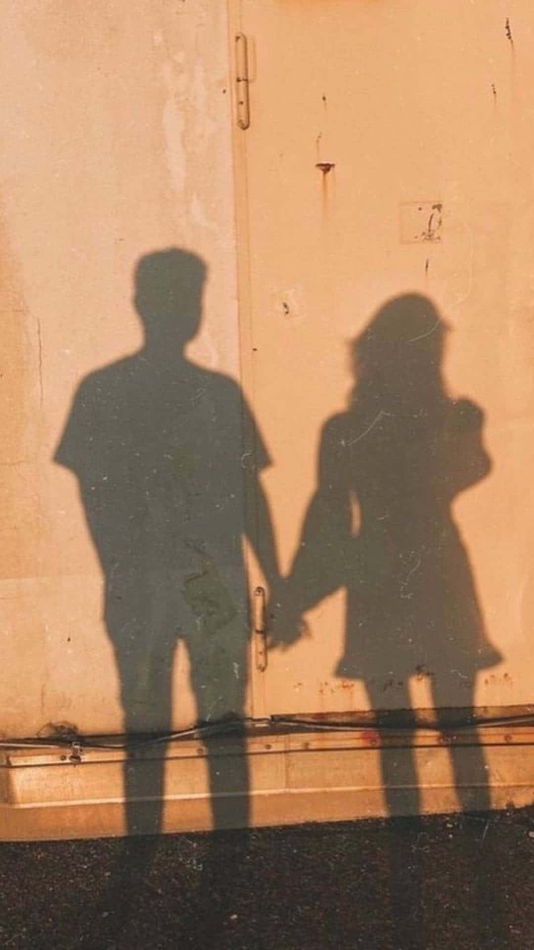 shadow 桌布 壁紙 — 一對情侶手牽手的剪影投射在經風化的牆上，沐浴在溫暖的金色光芒中。