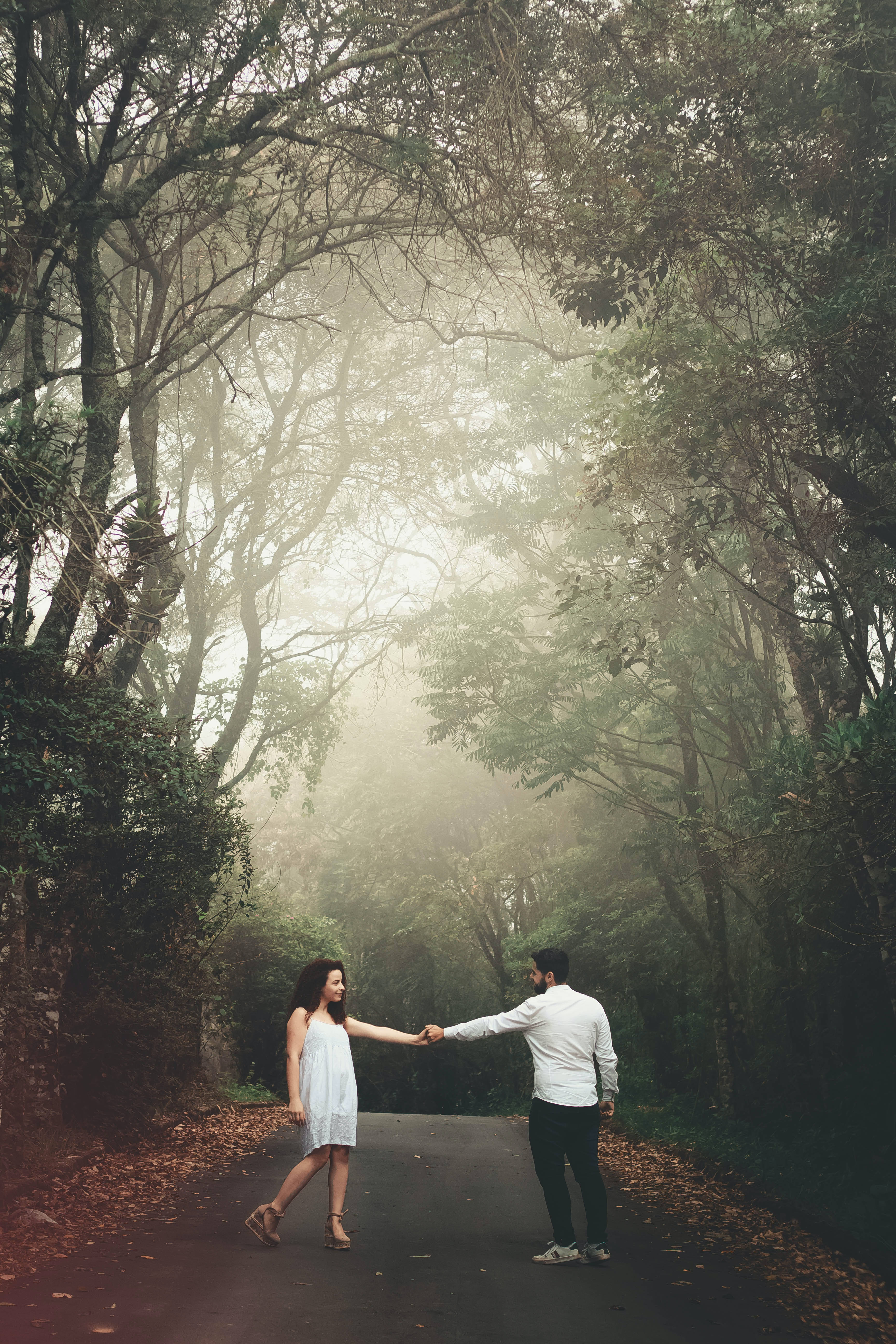 Lovers 桌布 壁紙 — 一對情侶手牽手走在一條霧氣瀰漫的森林小徑上，兩旁是高聳的樹木和落葉。
