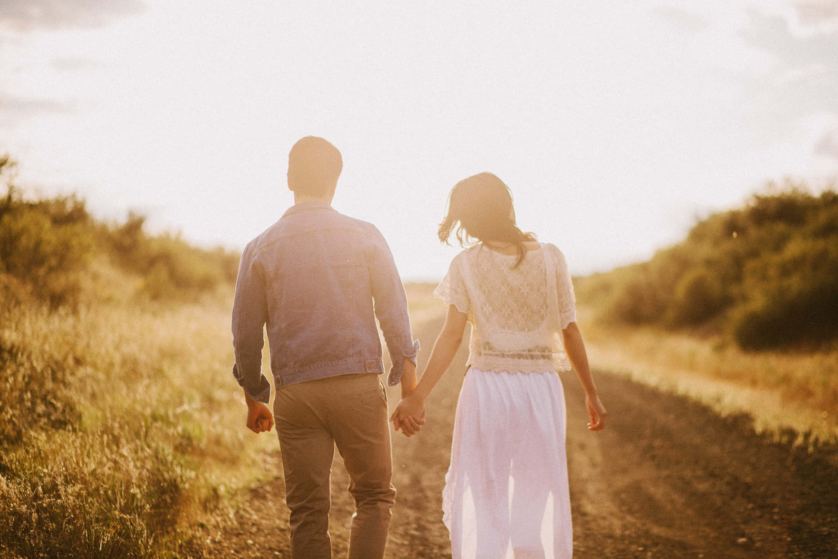 Couple Holding Hand 桌布 壁紙 — 一對情侶手牽手走在日落時分陽光灑落的金色草叢中的泥土小徑上。