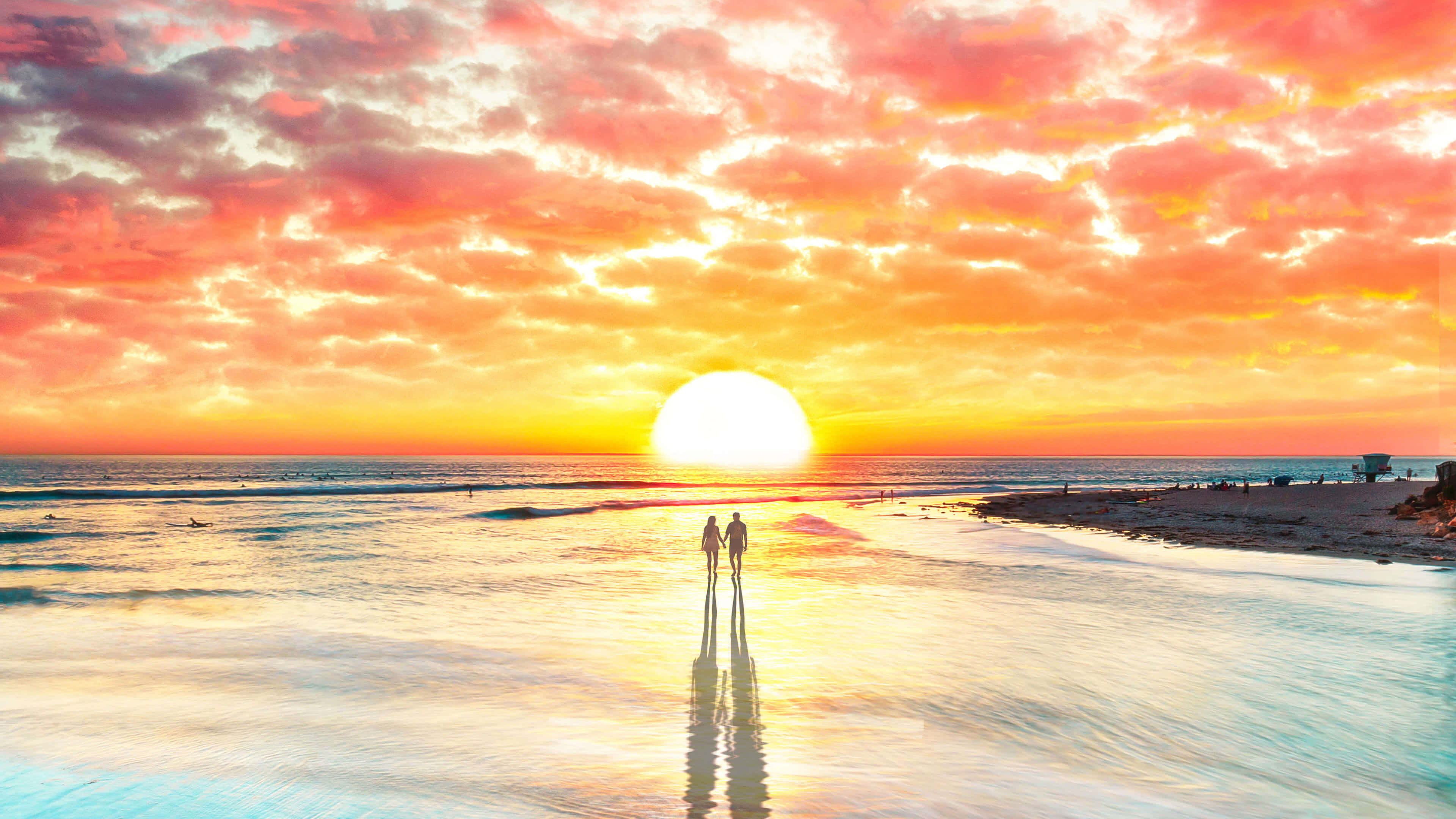 Beach Lovers 桌布 壁紙 — 一對情侶手牽手走在濕漉漉的海灘上，夕陽在火紅的橙色和粉紅色的天空中落下。
