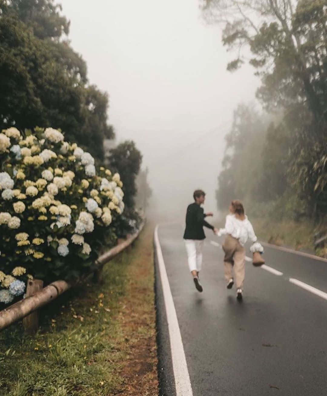 lover 桌布 壁紙 — 一對情侶手牽手跑在霧氣瀰漫的森林小路上，旁邊是鮮豔的繡球花叢。