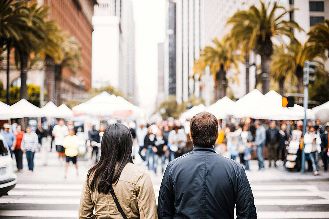 Love Cute Couple 桌布 壁紙 — 一對情侶沿著一條熙熙攘攘的市區街道走遠，街道兩旁種滿棕櫚樹和市場帳篷。