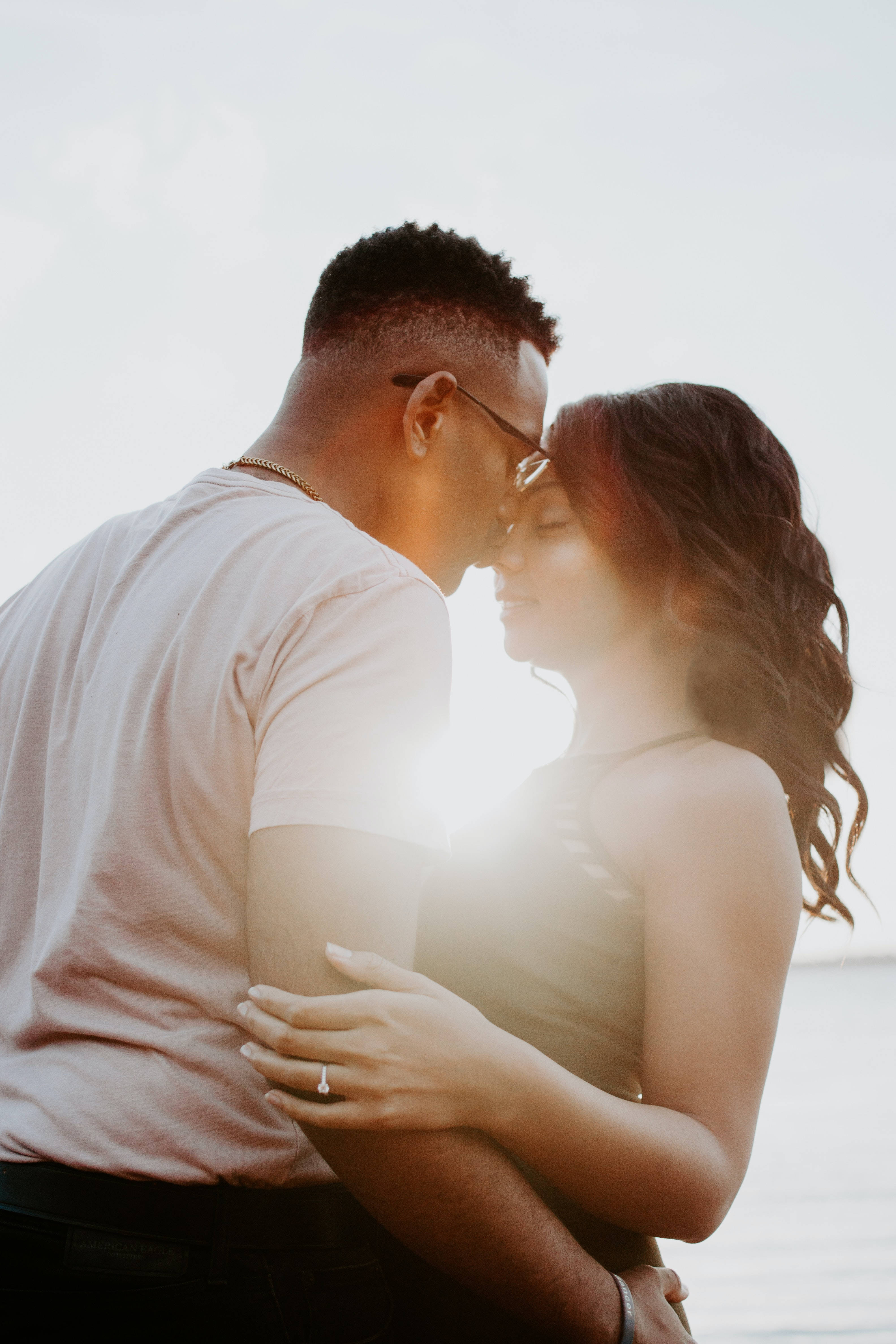 romantic kiss 桌布 壁紙 — 一對情侶溫柔地擁抱，金色的陽光在他們之間閃耀，映襯著柔和的天空。