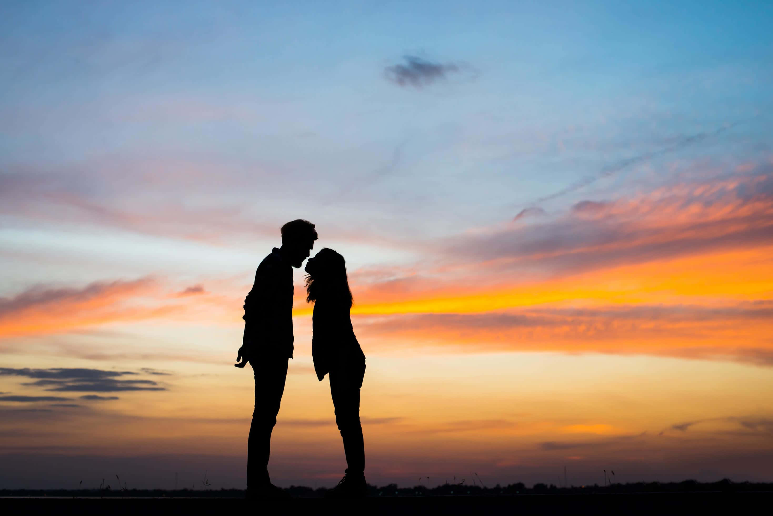 Kissing 桌布 壁紙 — 一對情侶的剪影在充滿活力的橙藍色夕陽天空下親密接吻。
