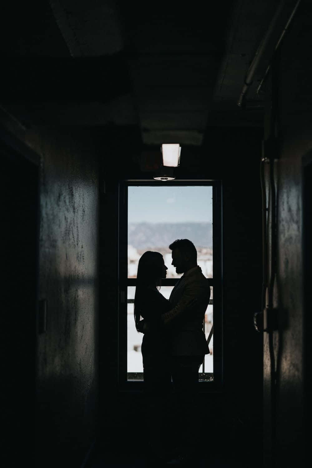 Black Couple 桌布 壁紙 — 一對情侶的剪影在昏暗的走廊中溫柔擁抱，窗框外展現出雪景。