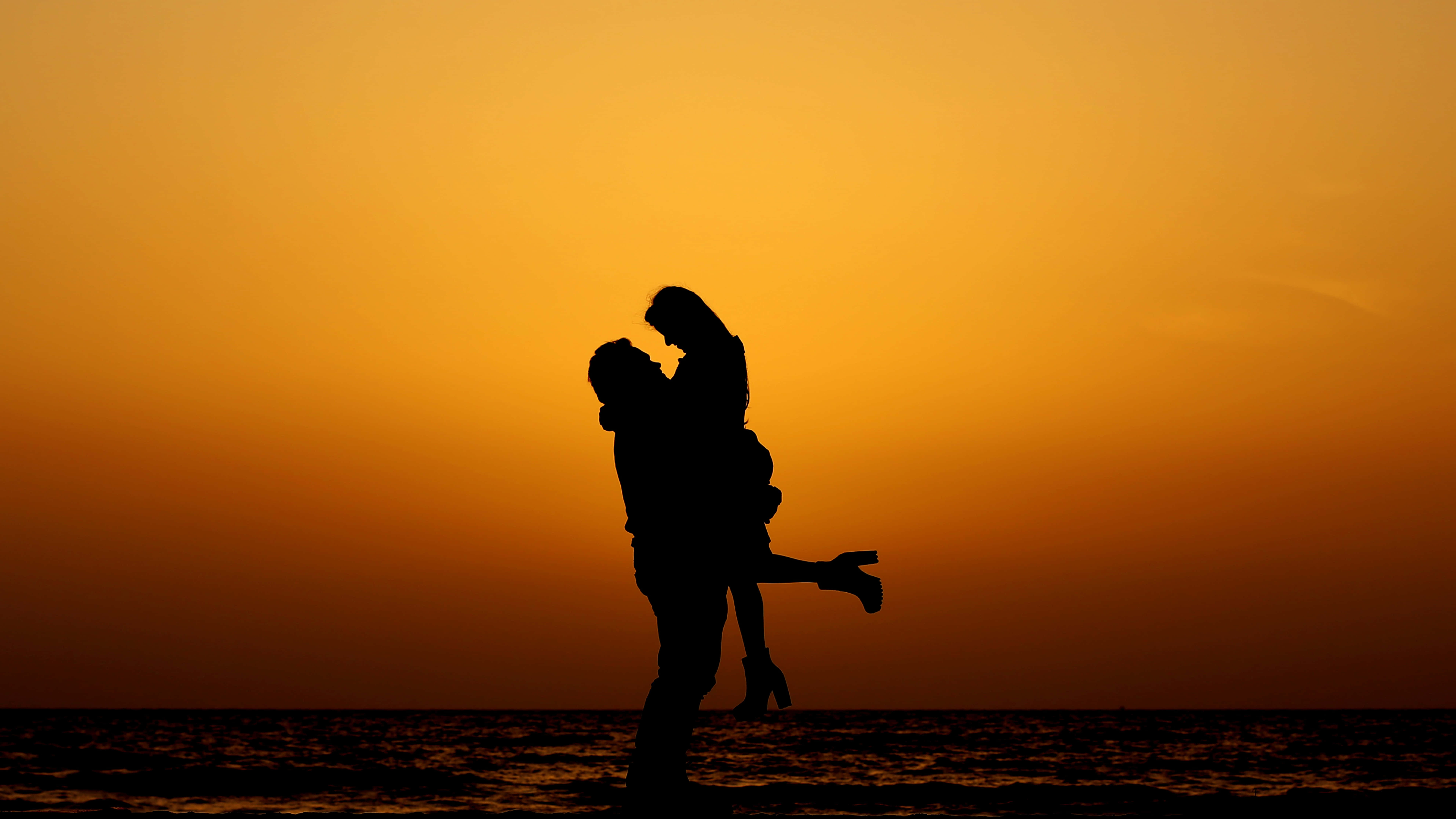 Beach Lovers 桌布 壁紙 — 一對情侶的剪影在海洋上熾熱的橙色日落中歡快地跳舞。