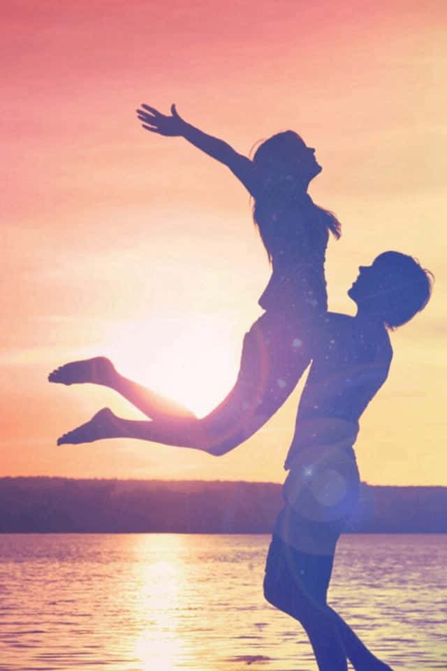 Silhouette 桌布 壁紙 — 一對情侶的剪影在閃爍的日落水面上歡樂跳躍，帶有鏡頭光暈。